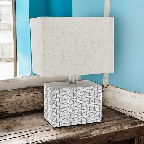 Table lamp with patterned base on a wooden surface against a blue wall.