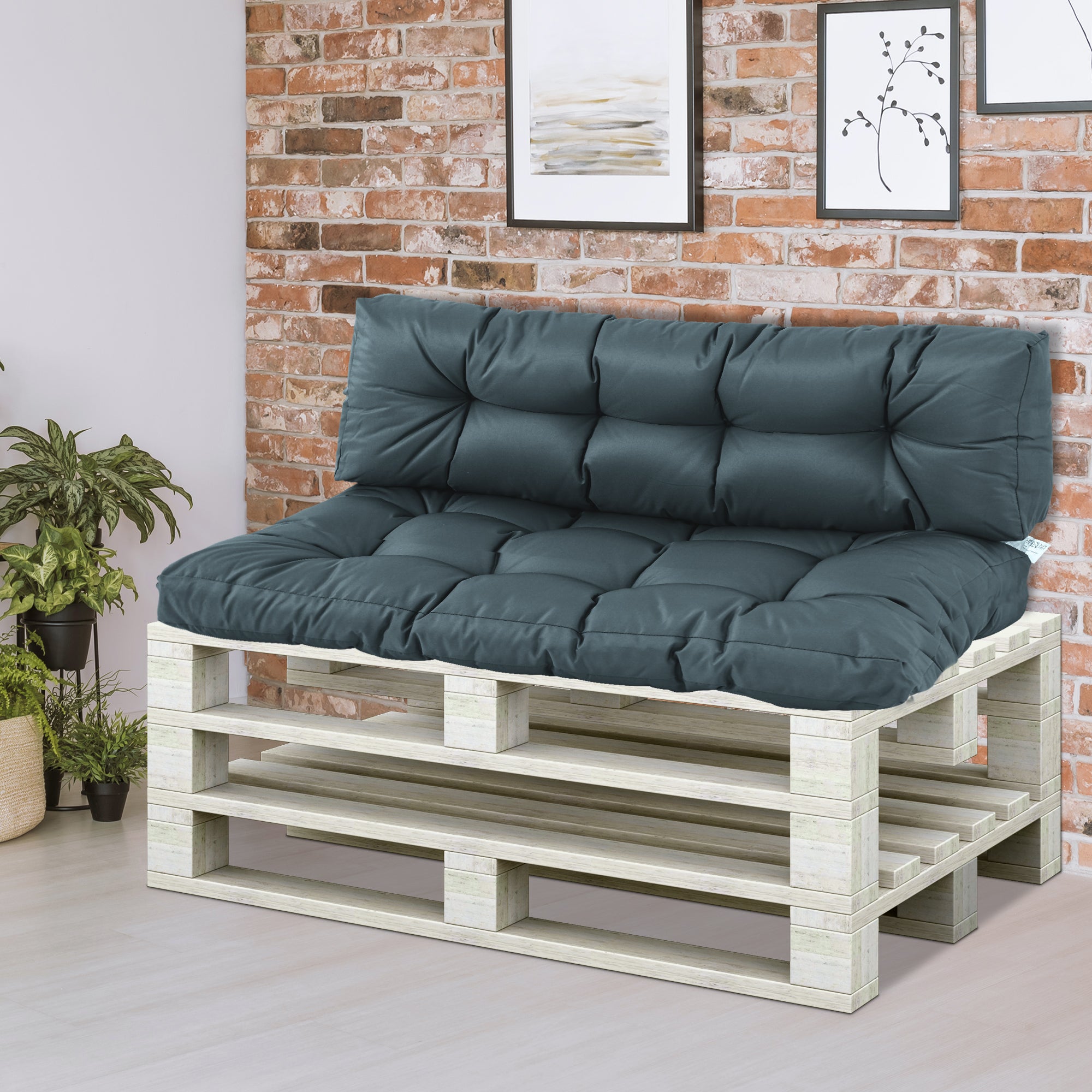 Wooden pallet bench with dark cushions against a brick wall.