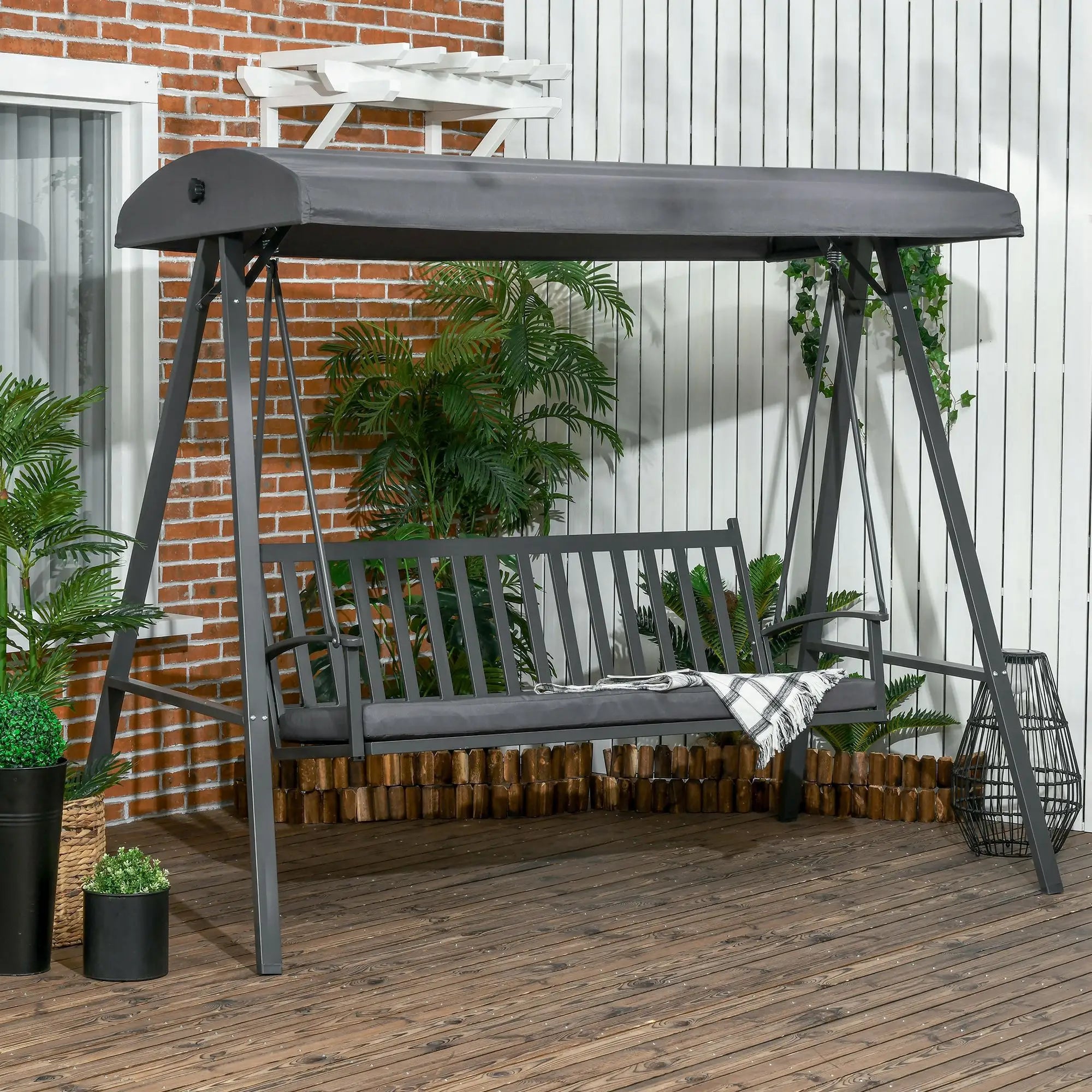 Garden swing with canopy on a wooden deck with plants and a brick wall in the background