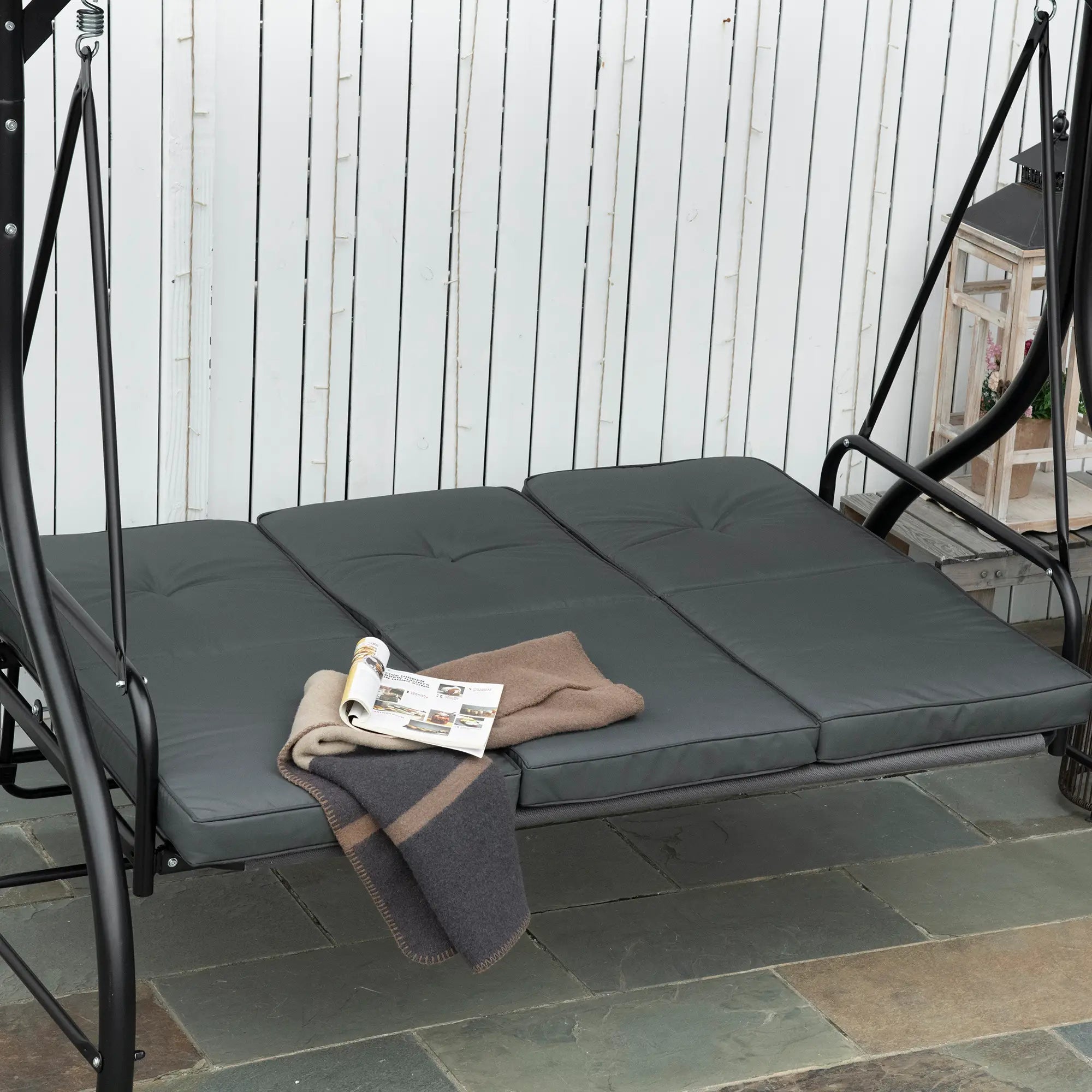 Gray outdoor swing with cushions and a blanket on a stone patio.