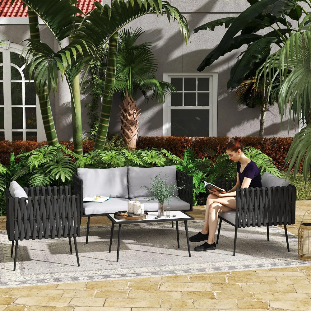 Outdoor patio with gray sofa, black chairs, and a small table with plants and a person using a tablet.