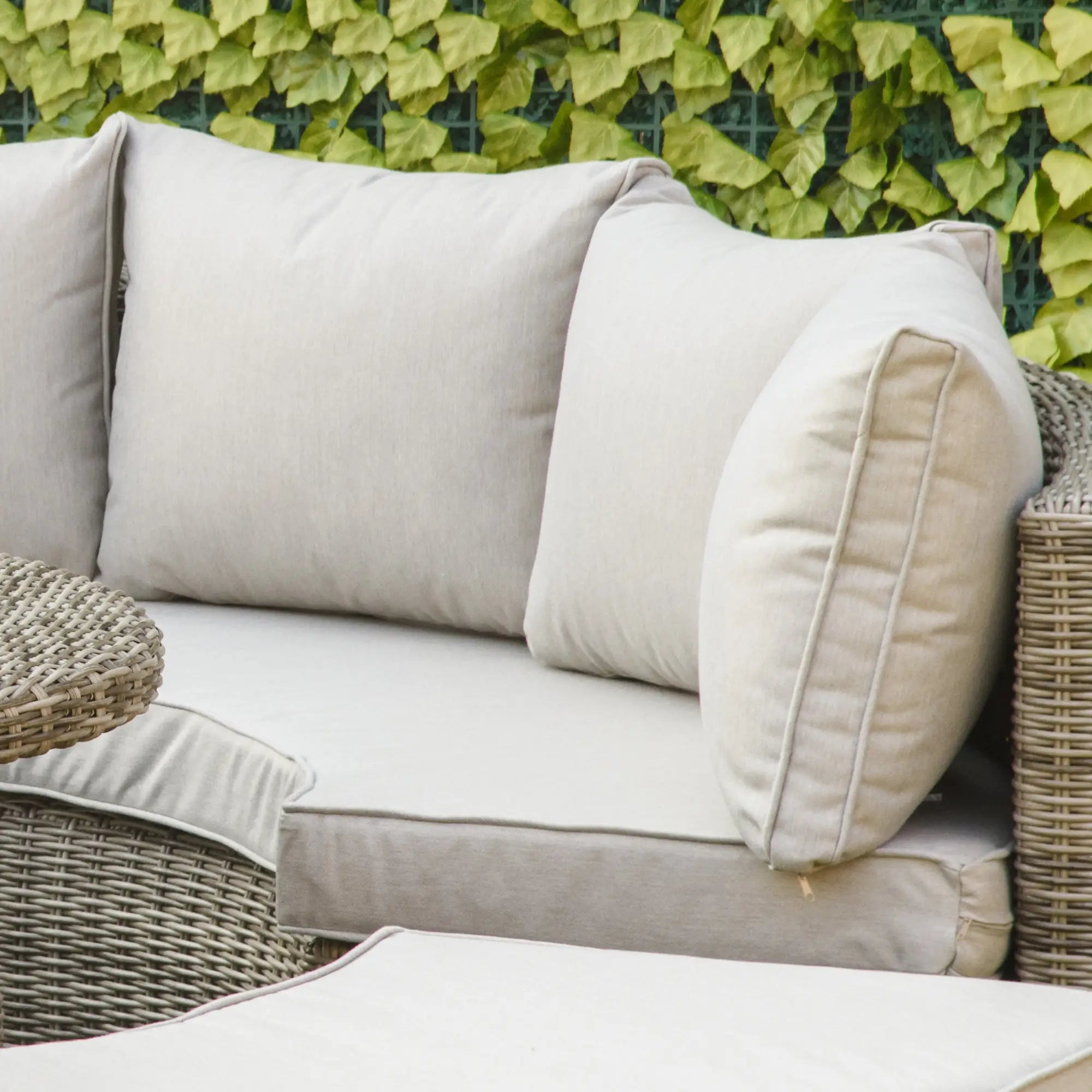 Beige outdoor sofa with cushions against a green leafy background