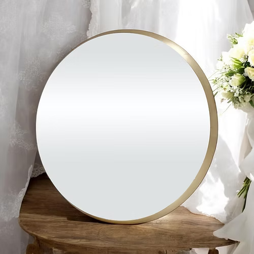 Round mirror with gold frame on a wooden surface with flowers in the background