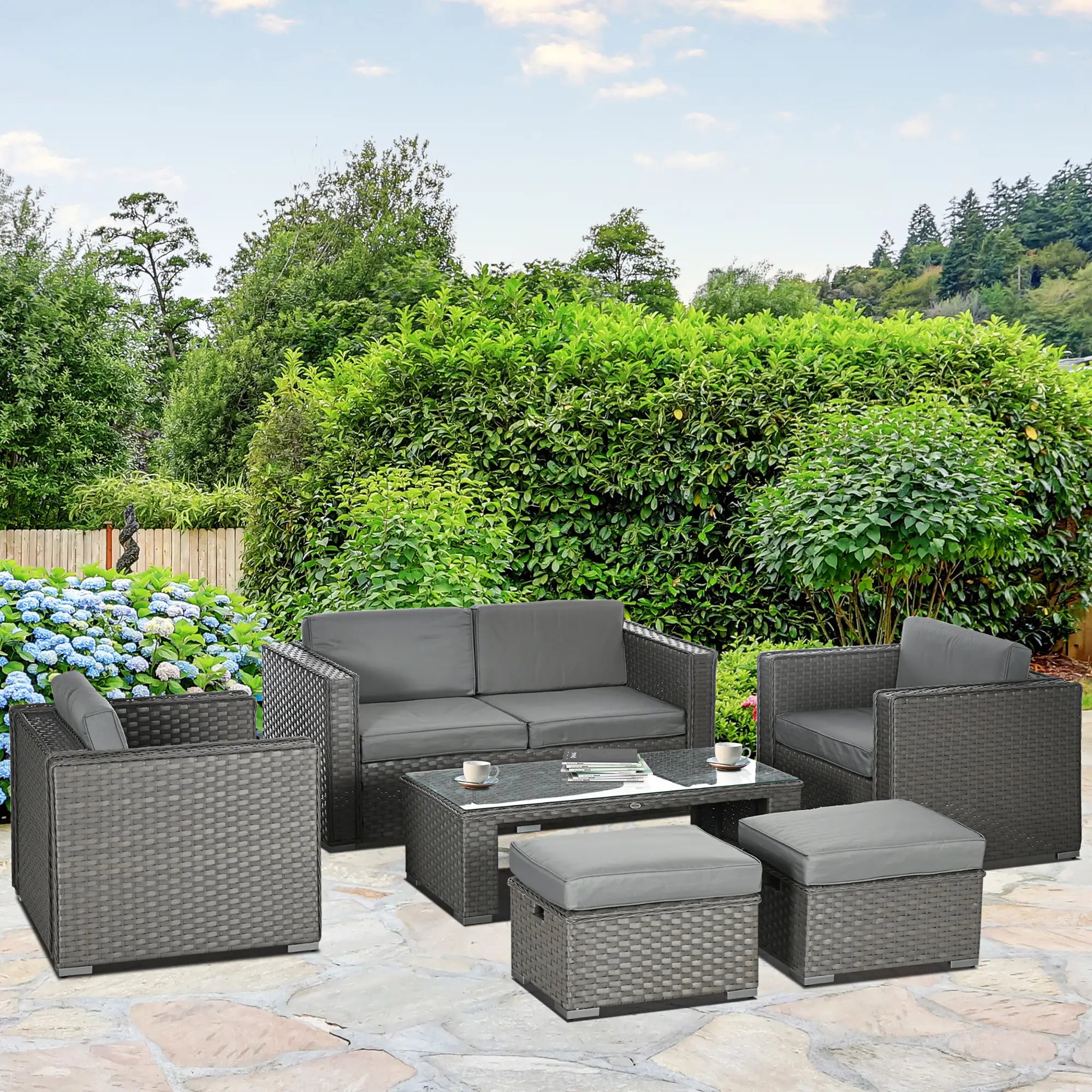 Outdoor patio furniture set with gray cushions on a stone patio, surrounded by greenery.