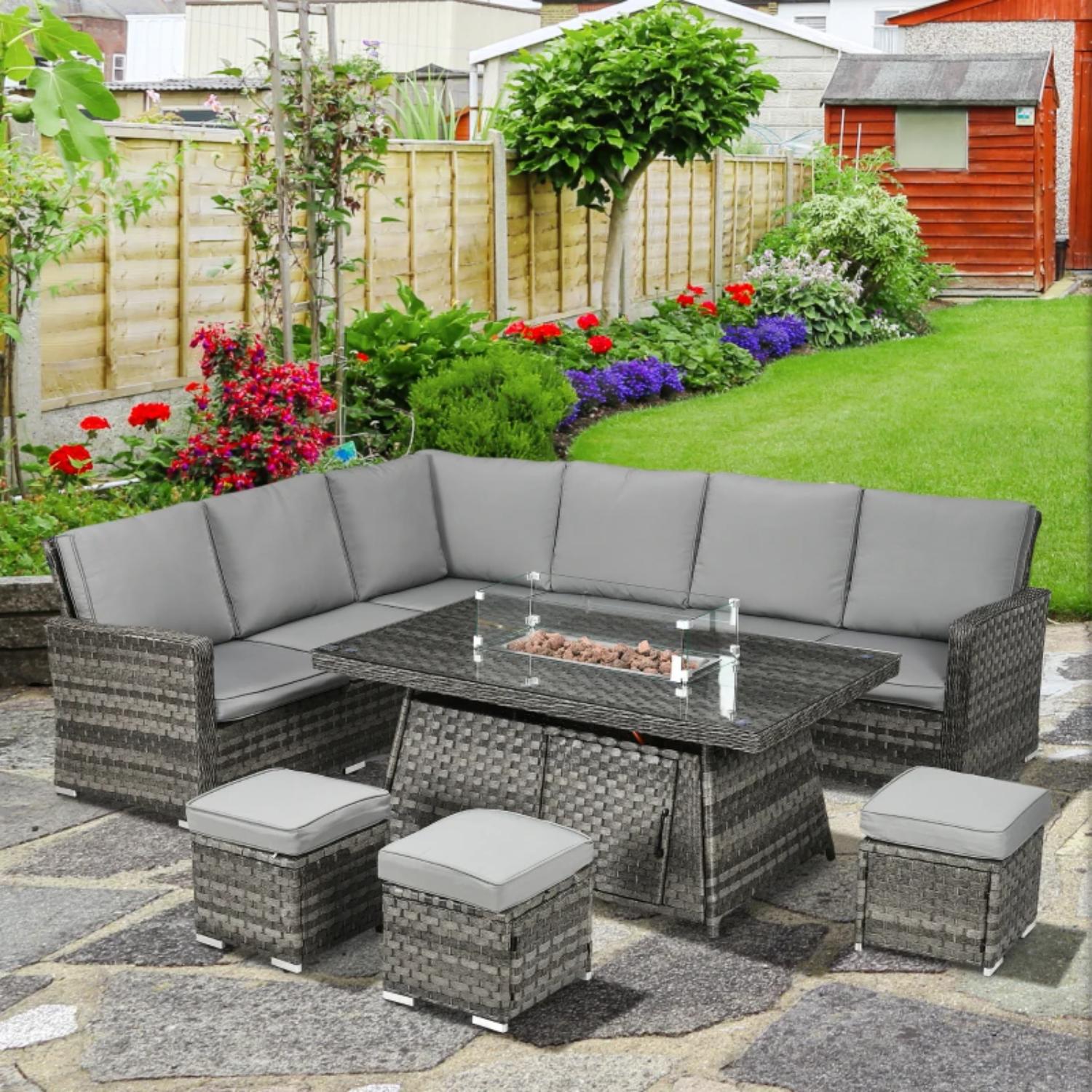 Outdoor patio set with gray cushions on a stone patio, surrounded by a garden with flowers and a wooden fence.