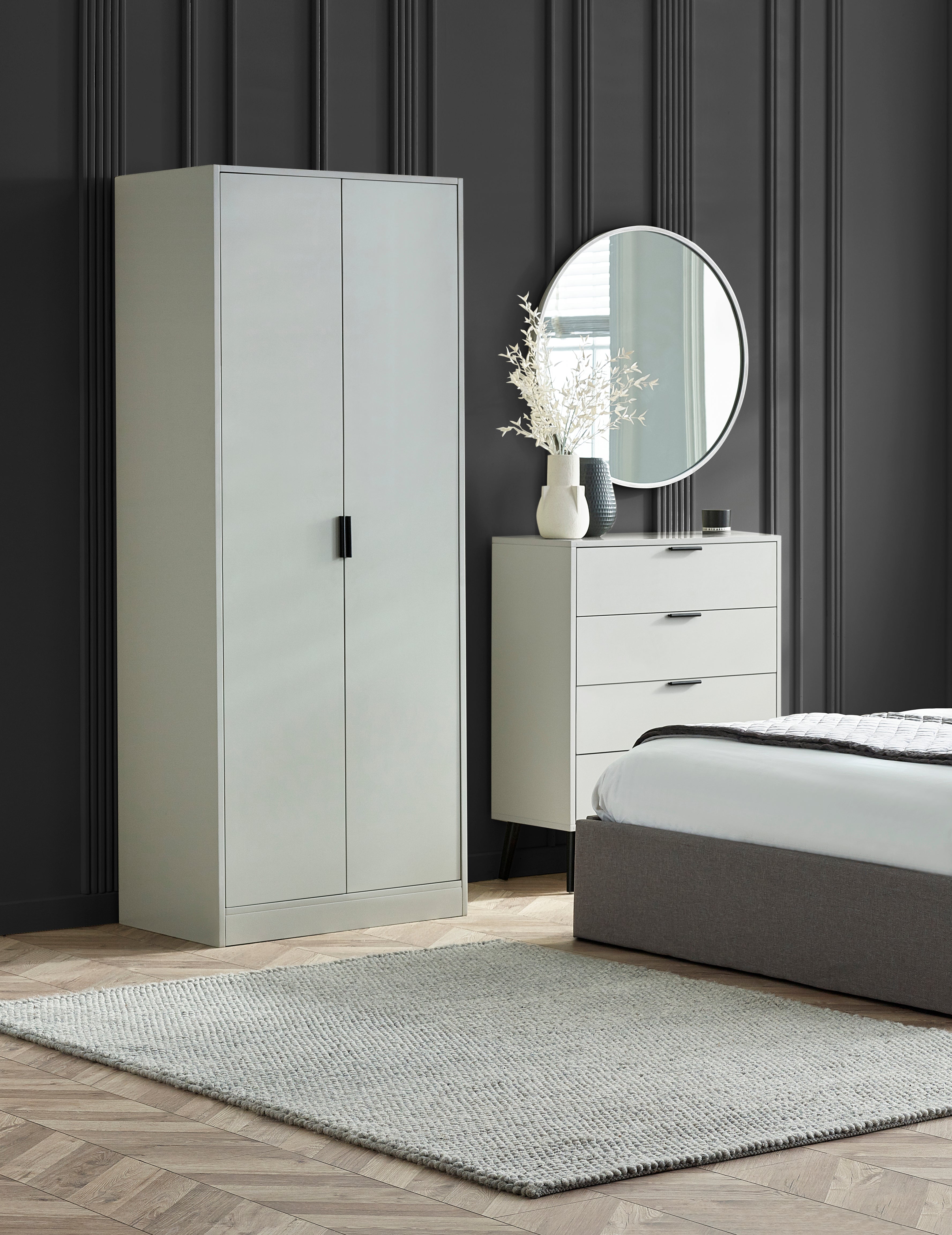 Modern bedroom with a light gray wardrobe, bed, and dresser against a dark paneled wall.