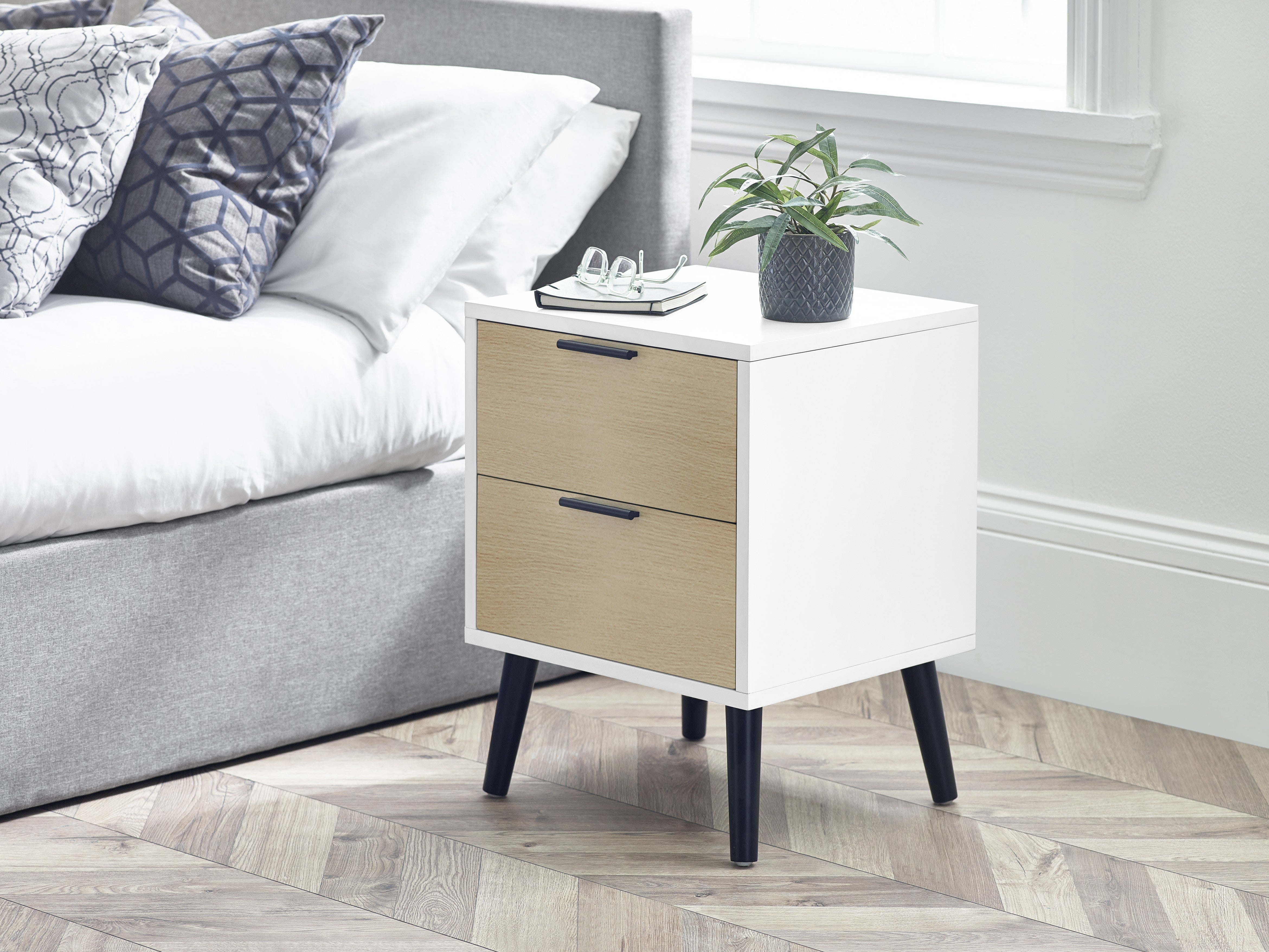 White and beige nightstand with two drawers next to a bed in a bedroom.