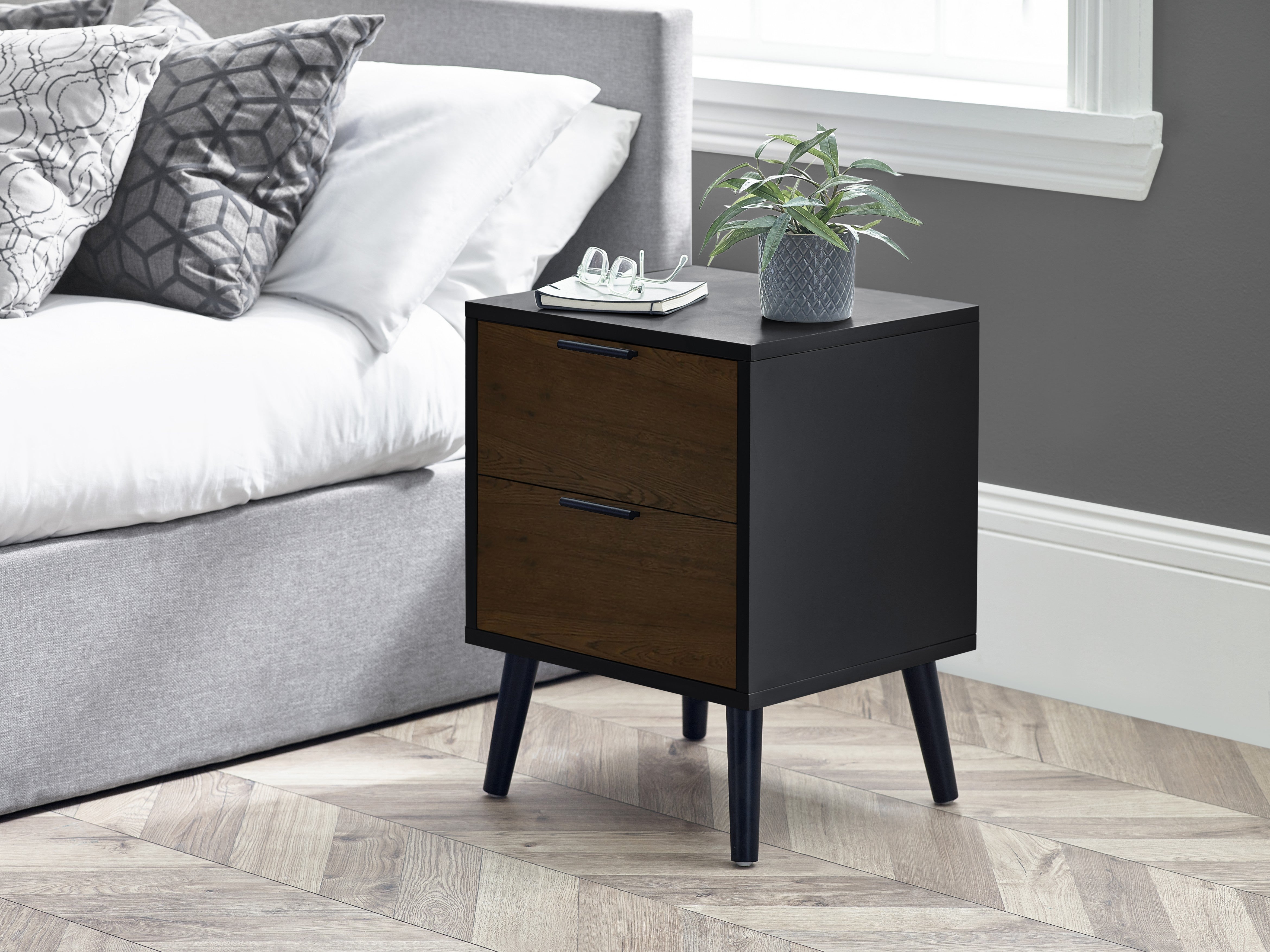 Black nightstand with two drawers next to a bed in a bedroom setting.