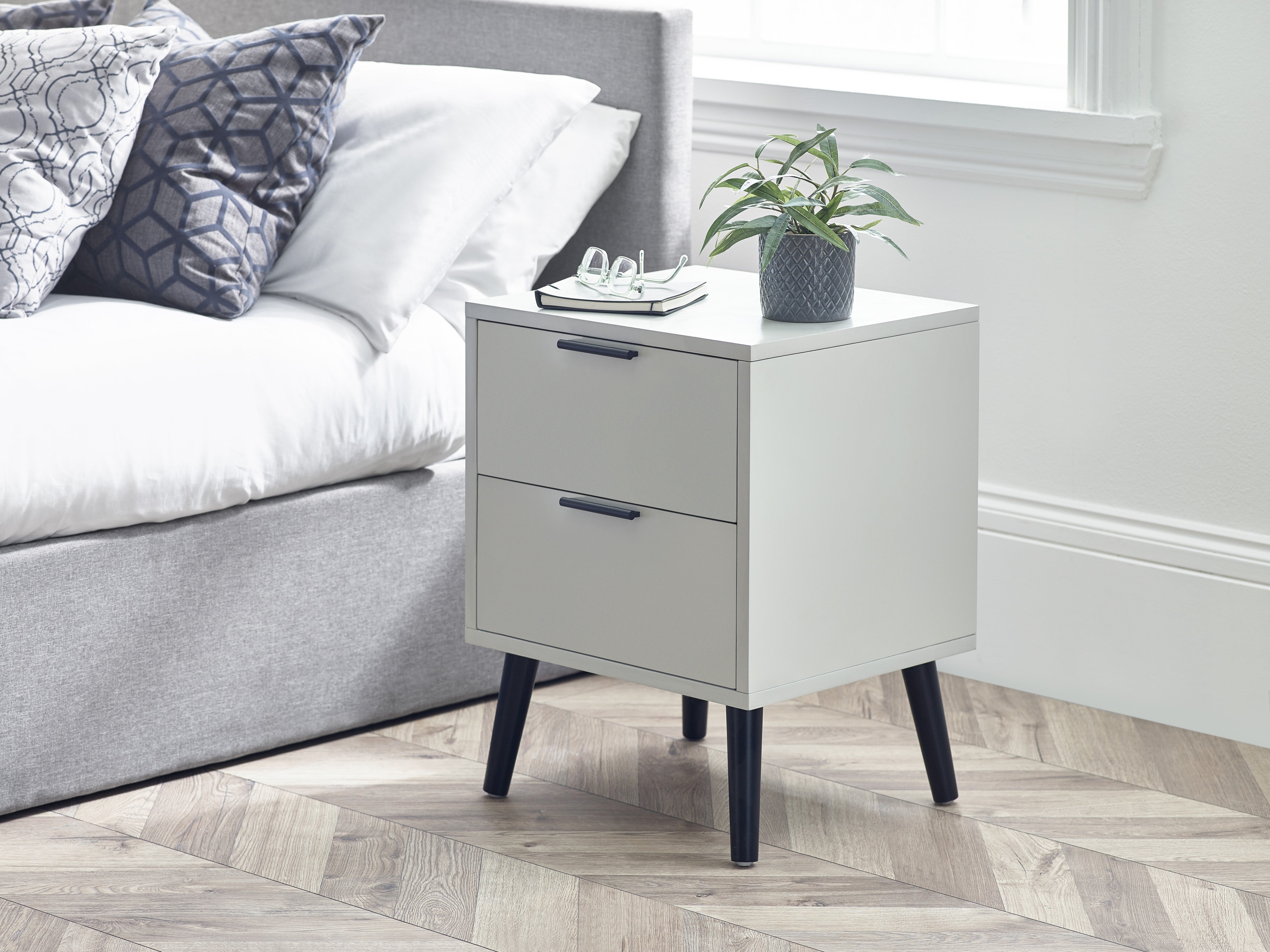 White nightstand with two drawers next to a bed in a bedroom setting.