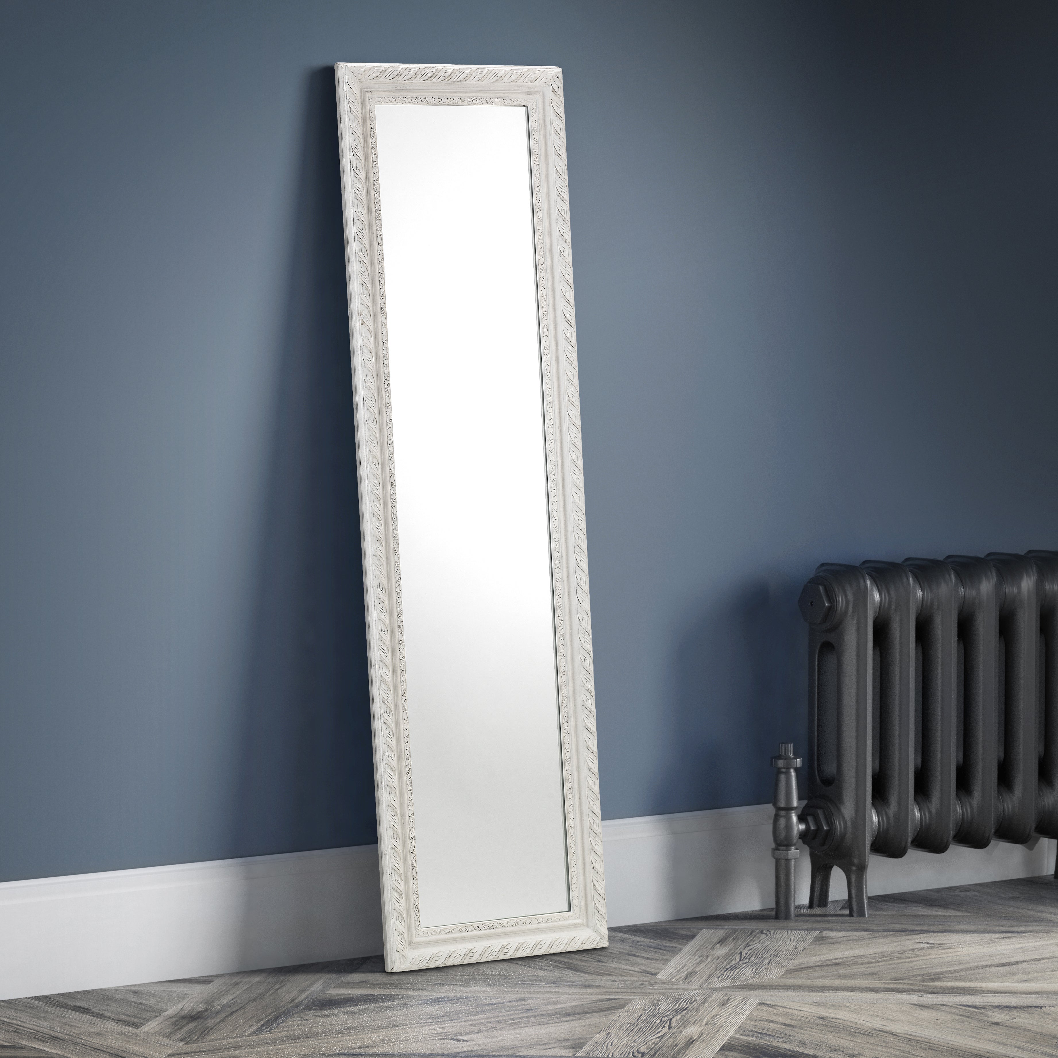 White floor mirror leaning against a blue wall with a radiator in the background.