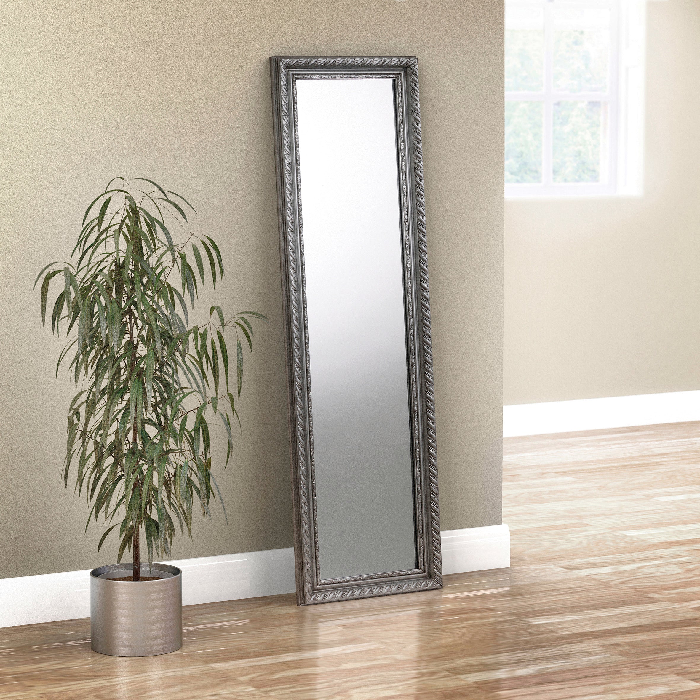 Tall floor mirror with decorative frame next to a potted plant on a wooden floor.