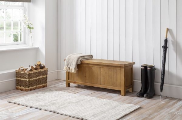 Wooden bench with a rug, wicker basket, and boots in a room with white walls and a window.