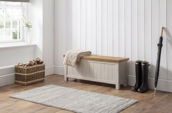 Wooden bench with a blanket, basket, and boots in a room with white walls and wooden flooring.