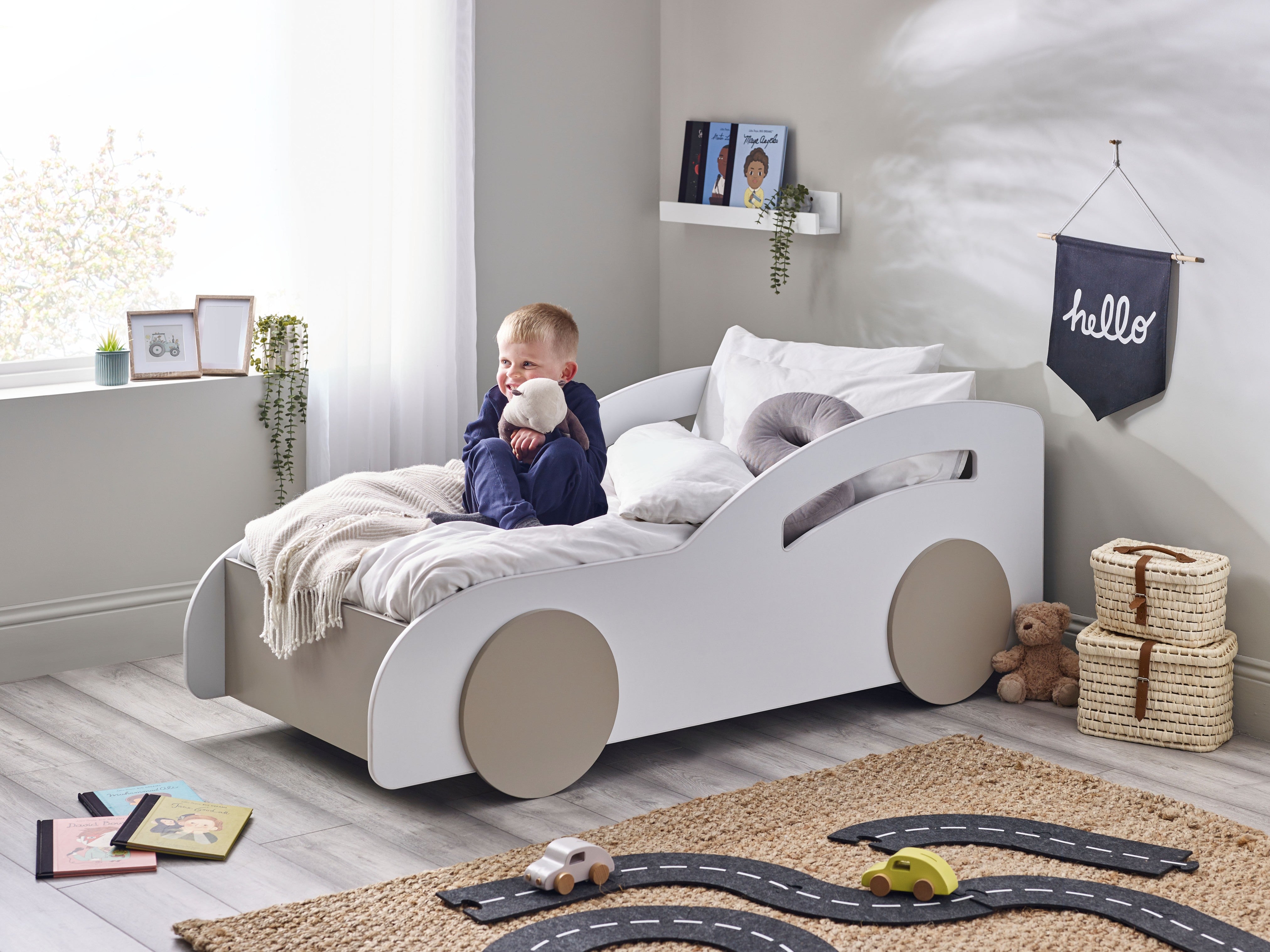 Child in a car-shaped bed with toys and decor in a room.