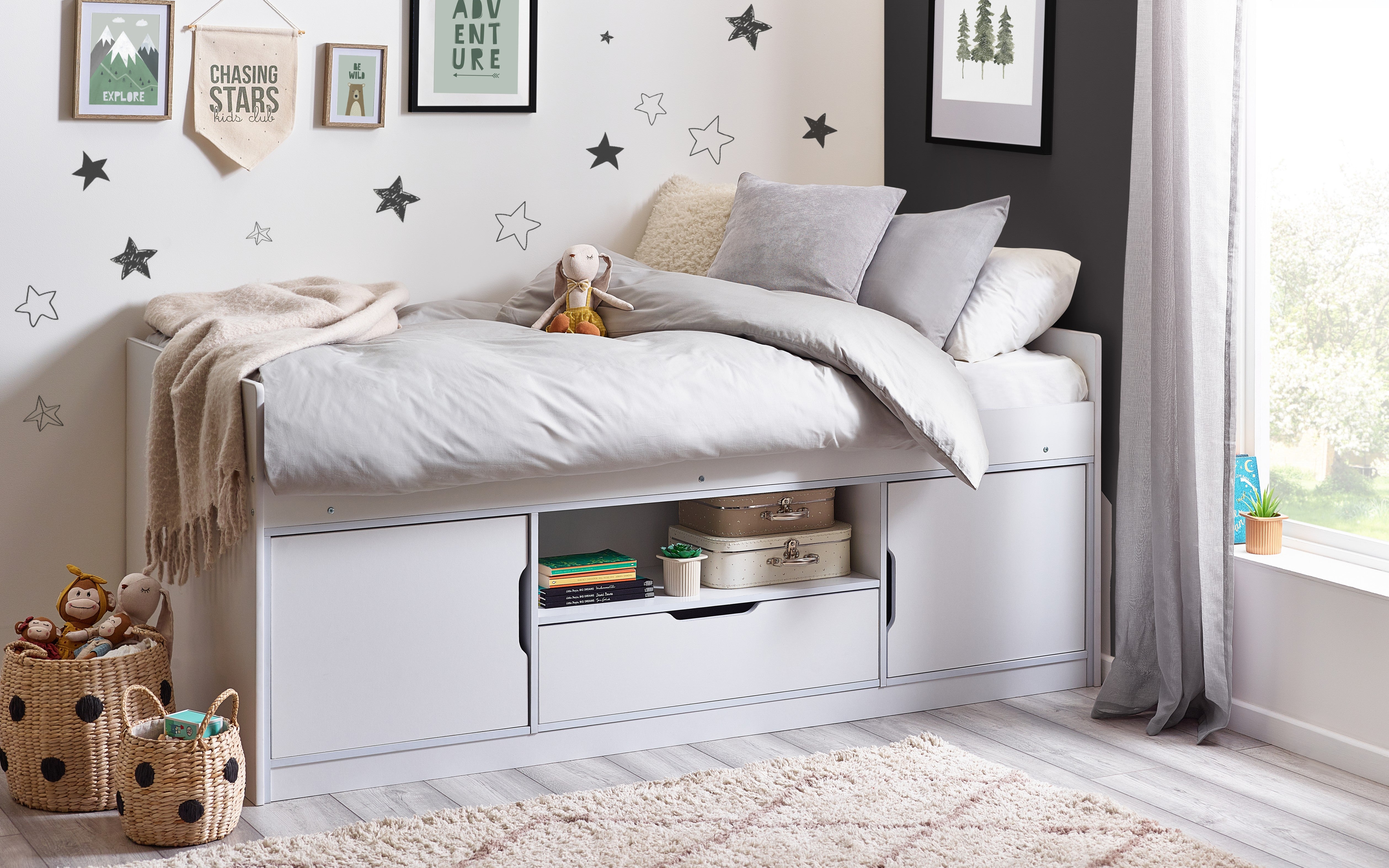 Children's bedroom with a white bed, storage drawers, and decorative elements.
