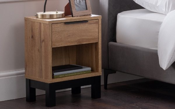 Wooden nightstand with books and a lamp next to a bed