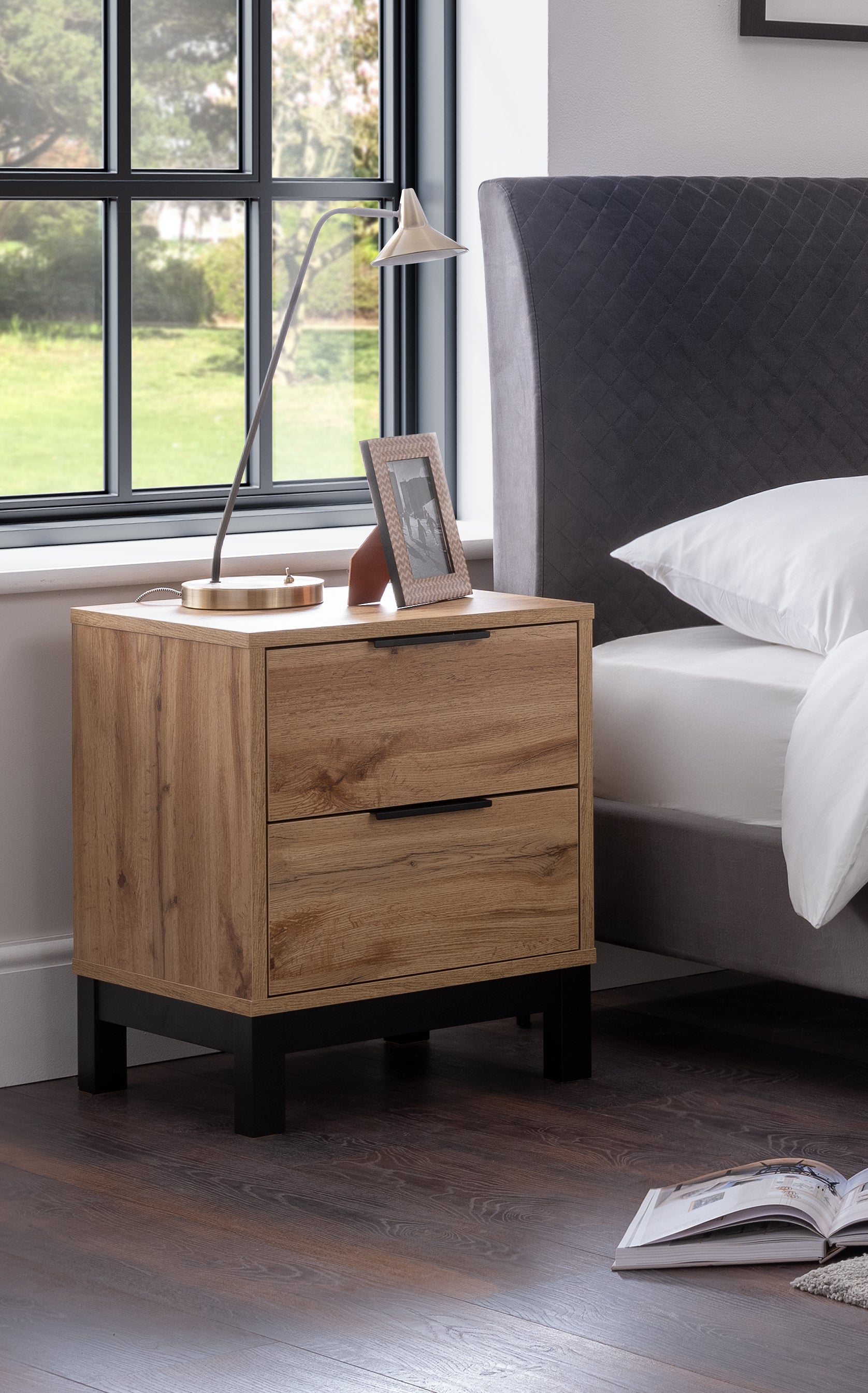 Wooden nightstand with two drawers next to a bed in a bedroom.