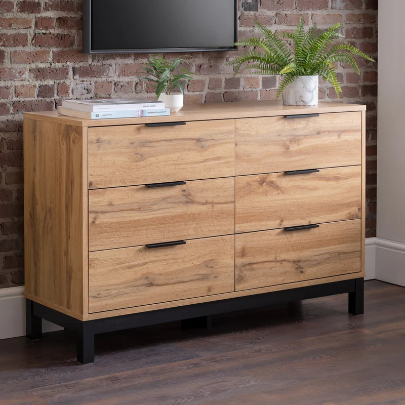 Wooden dresser with black handles against a brick wall.