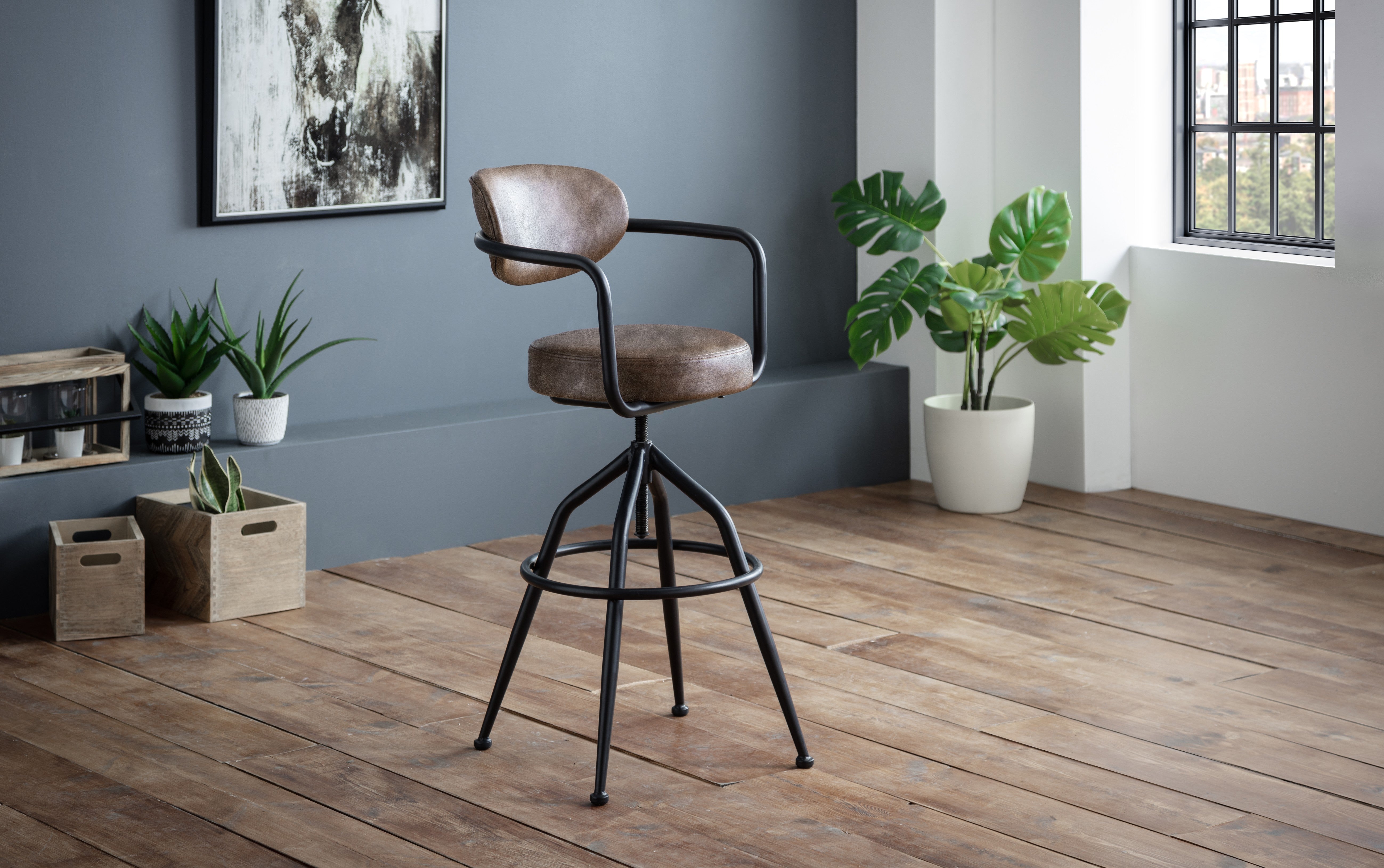Bar stool with brown leather seat and black metal frame in a room with plants and a window.