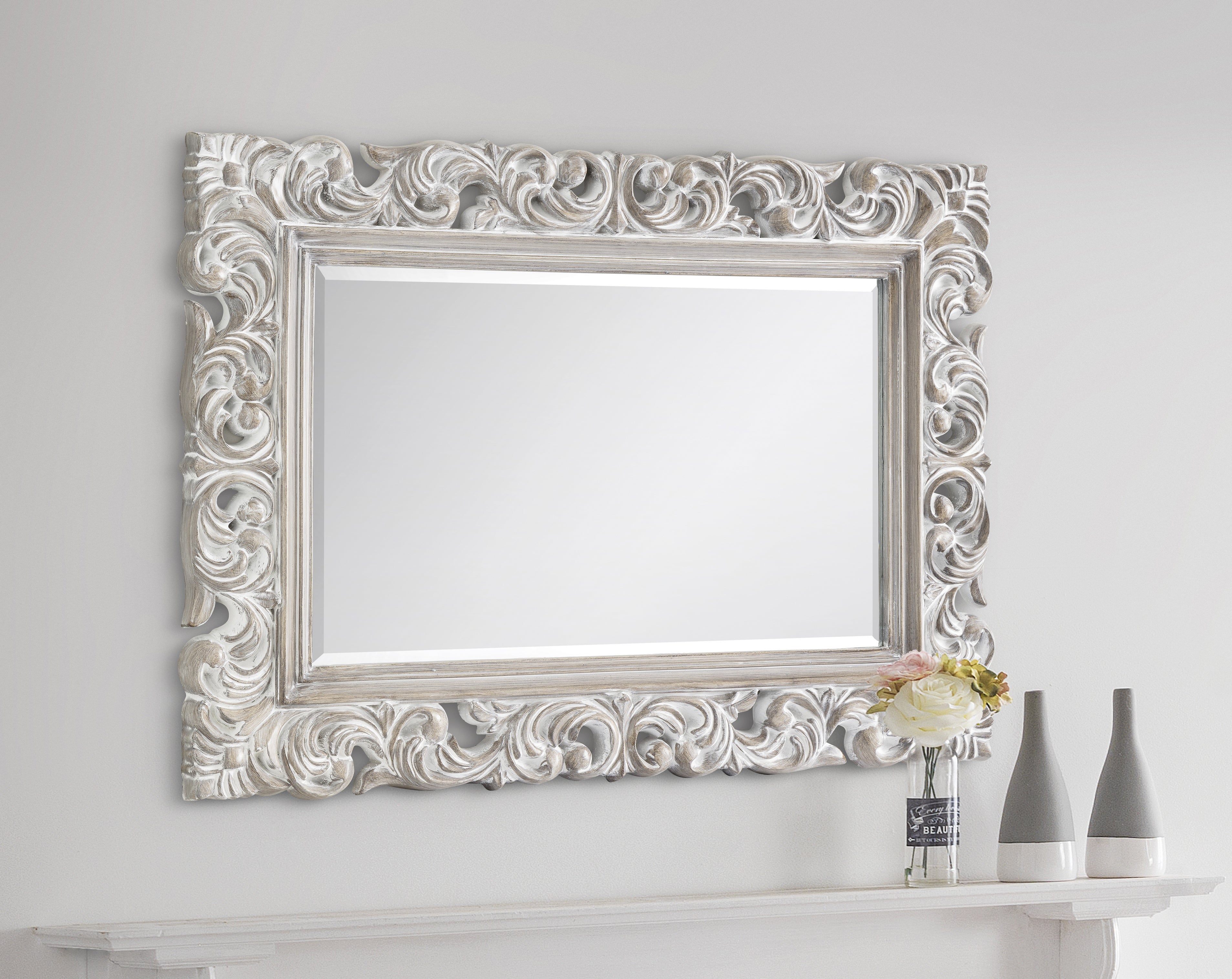Decorative wall mirror with intricate white frame on a plain white wall.