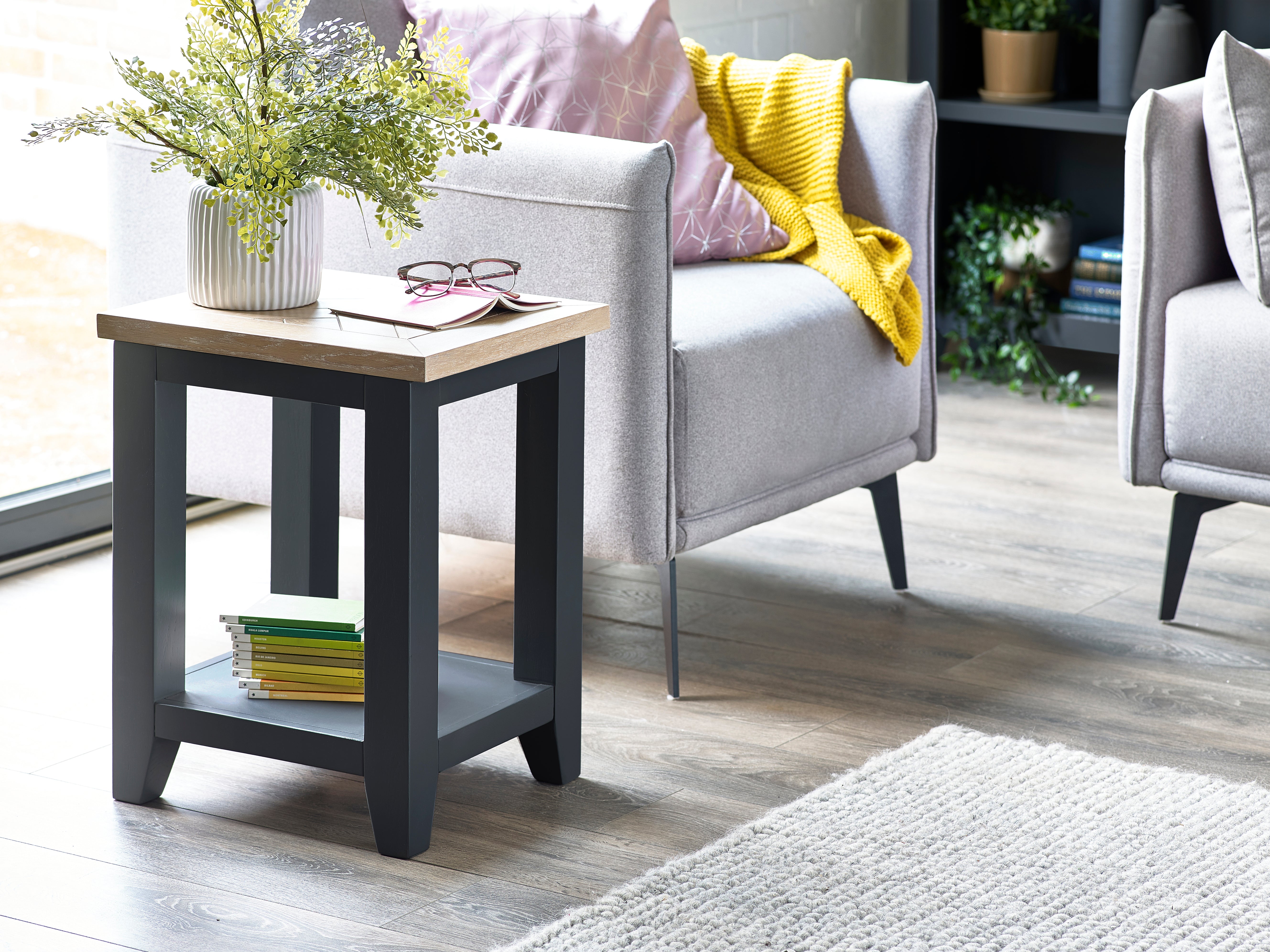 Small side table with a plant and books next to a gray armchair in a living room.