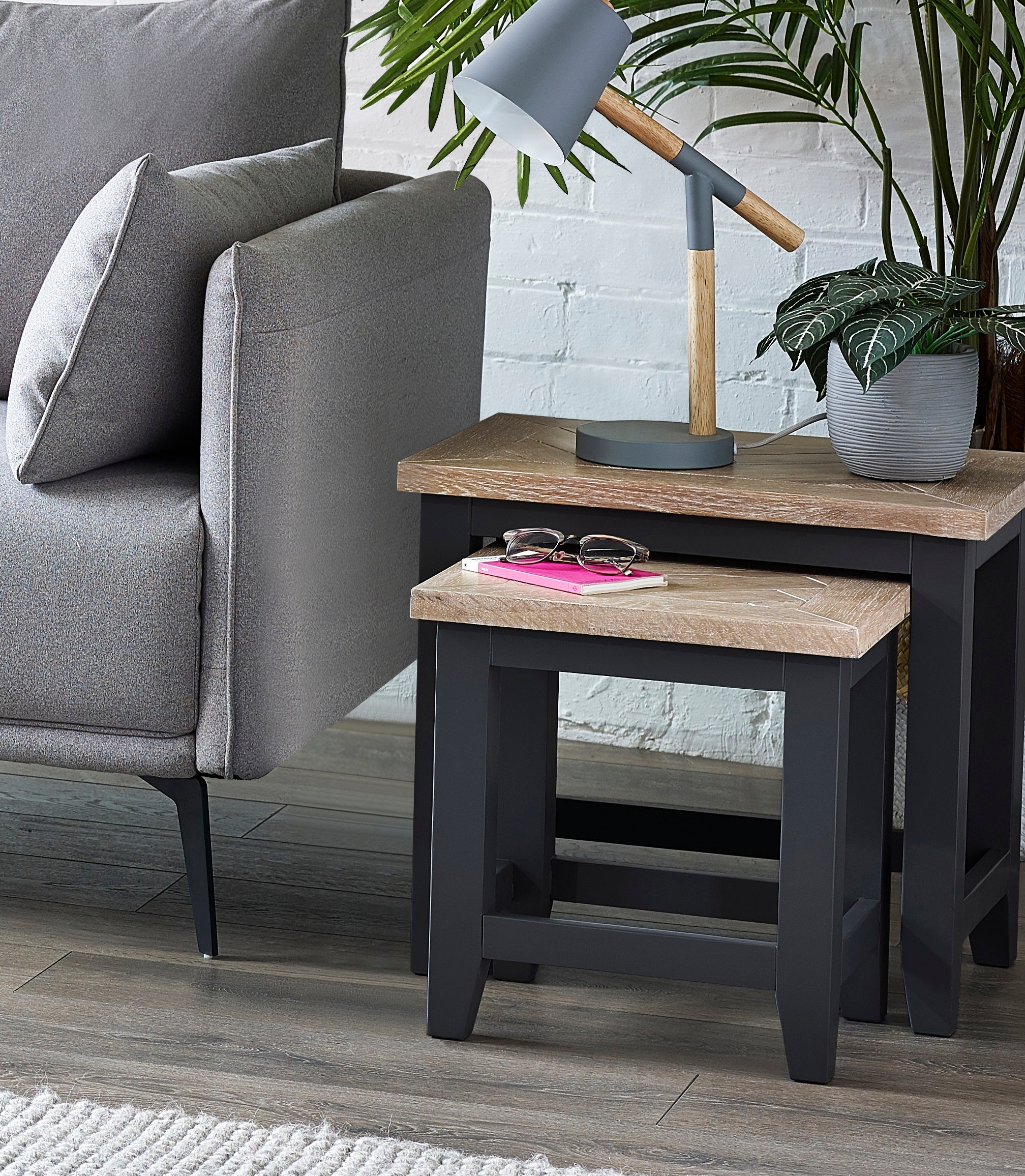 Two wooden side tables with a lamp and sunglasses next to a gray sofa.