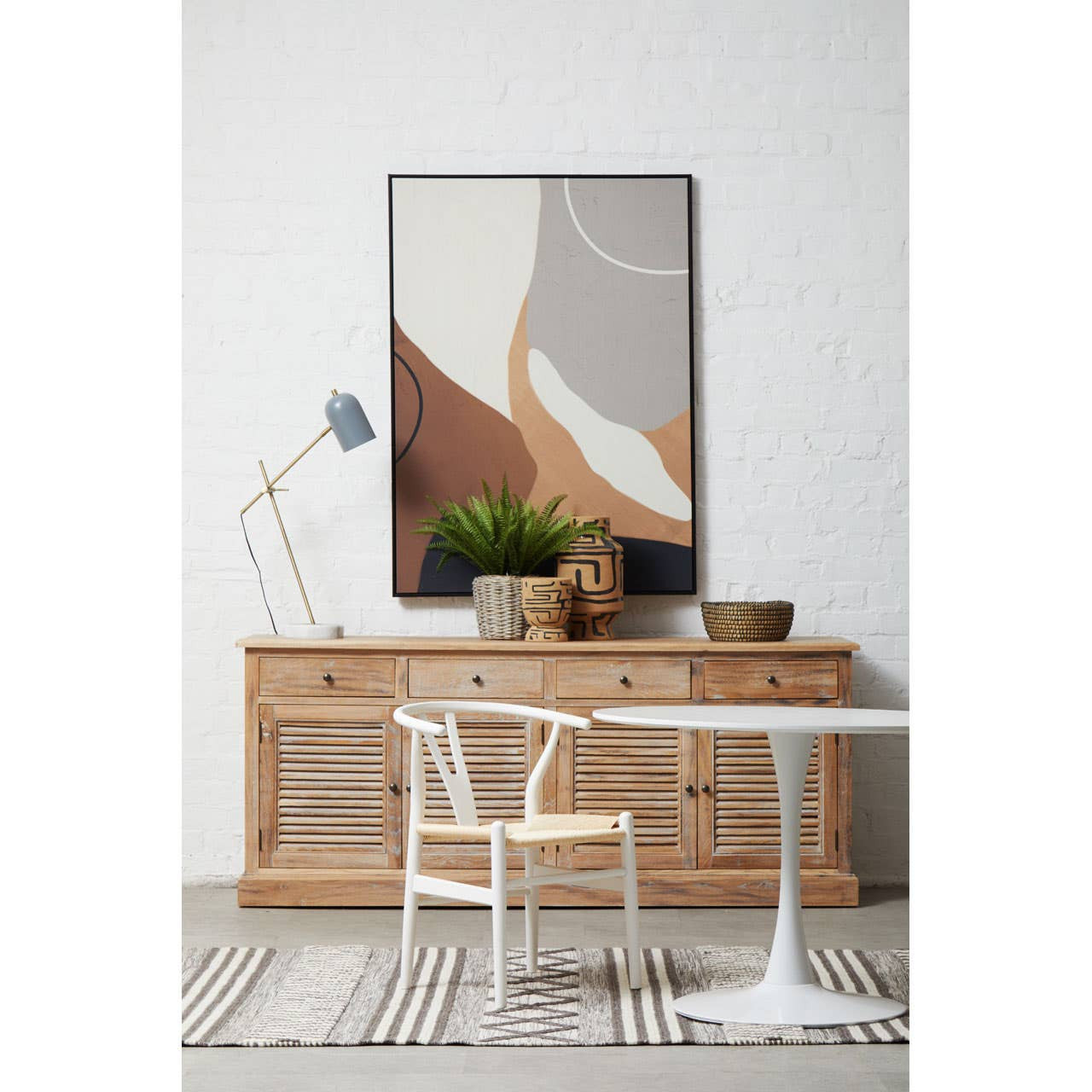 Modern interior with wooden sideboard, white chair, and abstract art on a white wall.