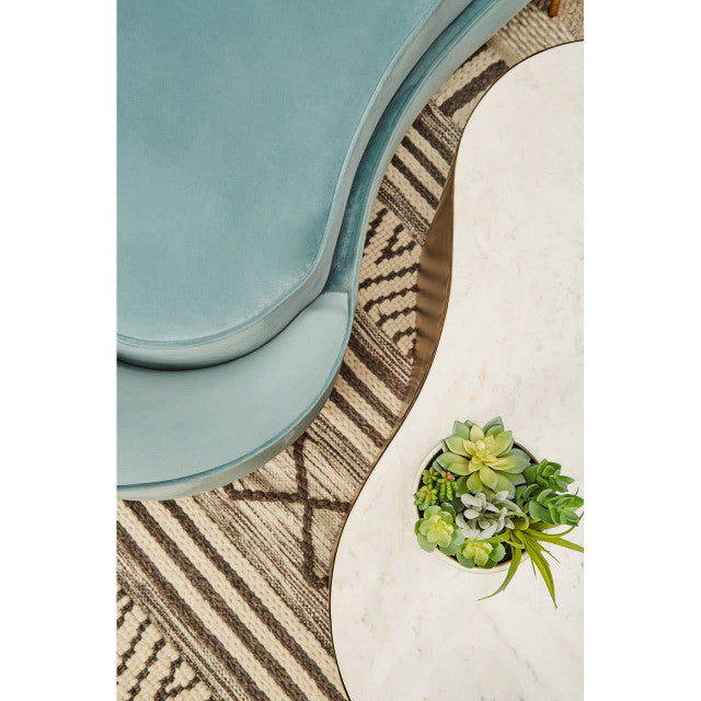 Light blue chair on a patterned rug with a white table and green plant.