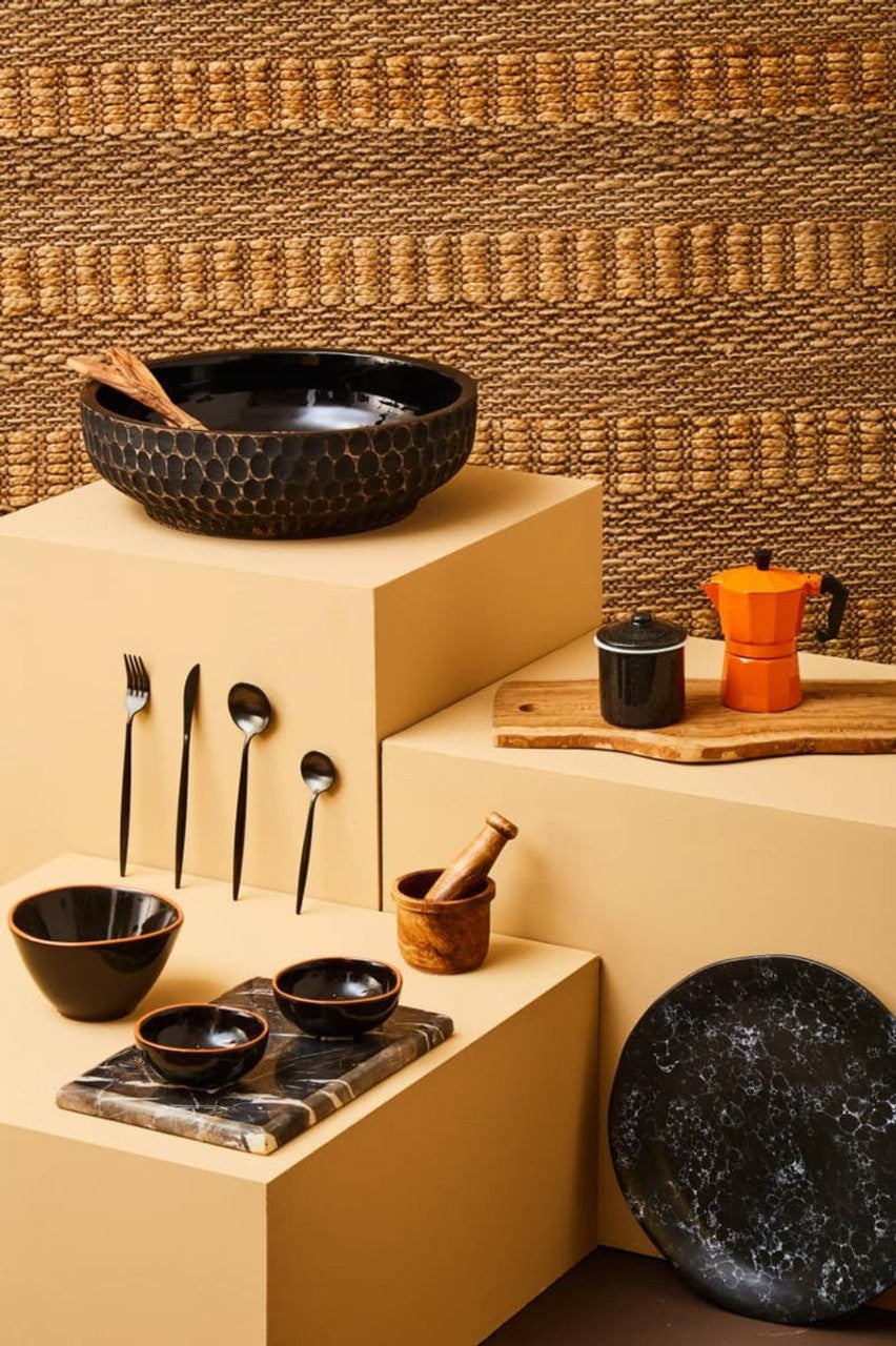 Set of black ceramic bowls and kitchen utensils on beige shelves against a textured brown wall.