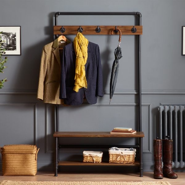 Clothing rack with coats, a yellow jacket, and an umbrella against a gray wall.
