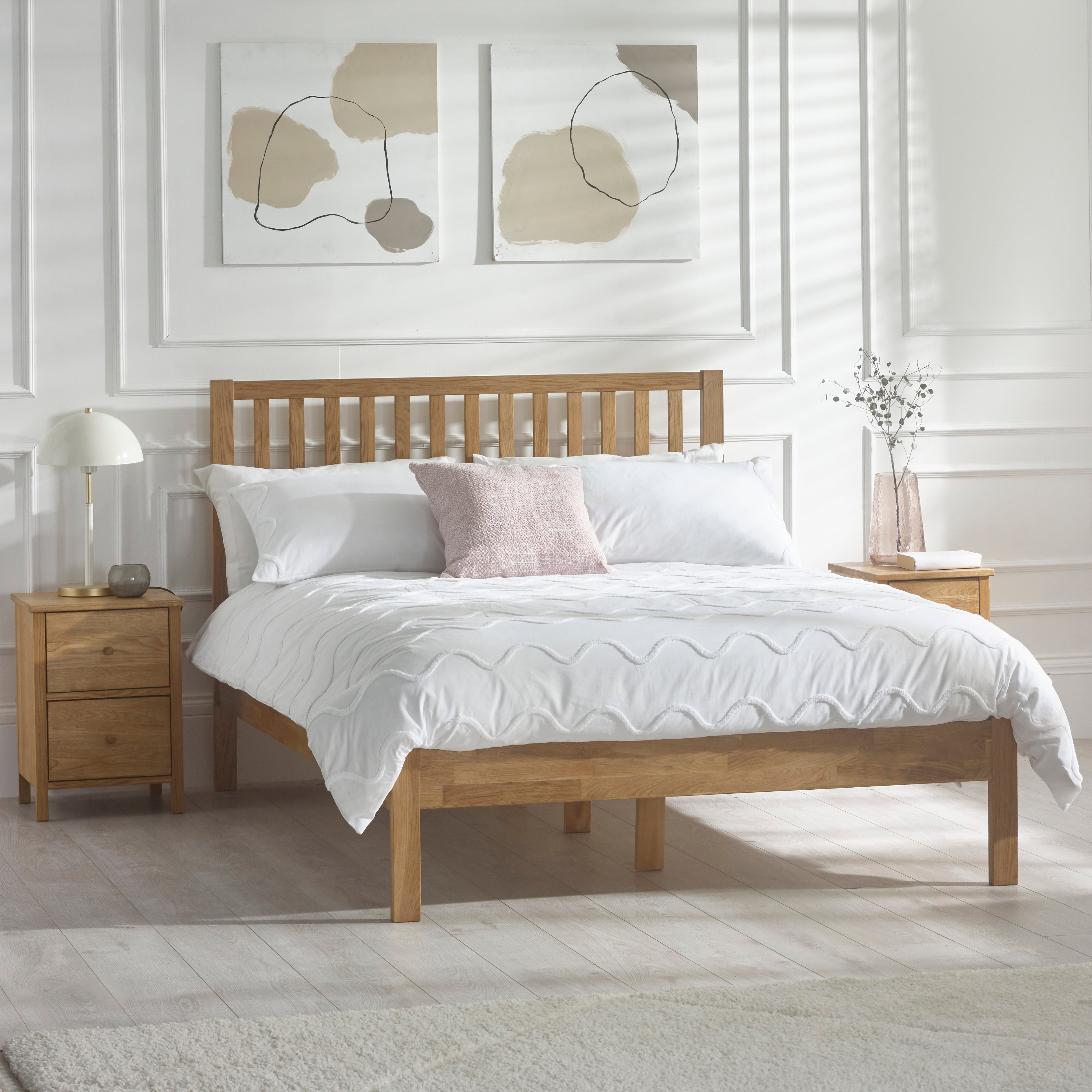 Wooden bed with white bedding in a bedroom setting with abstract art on the wall.