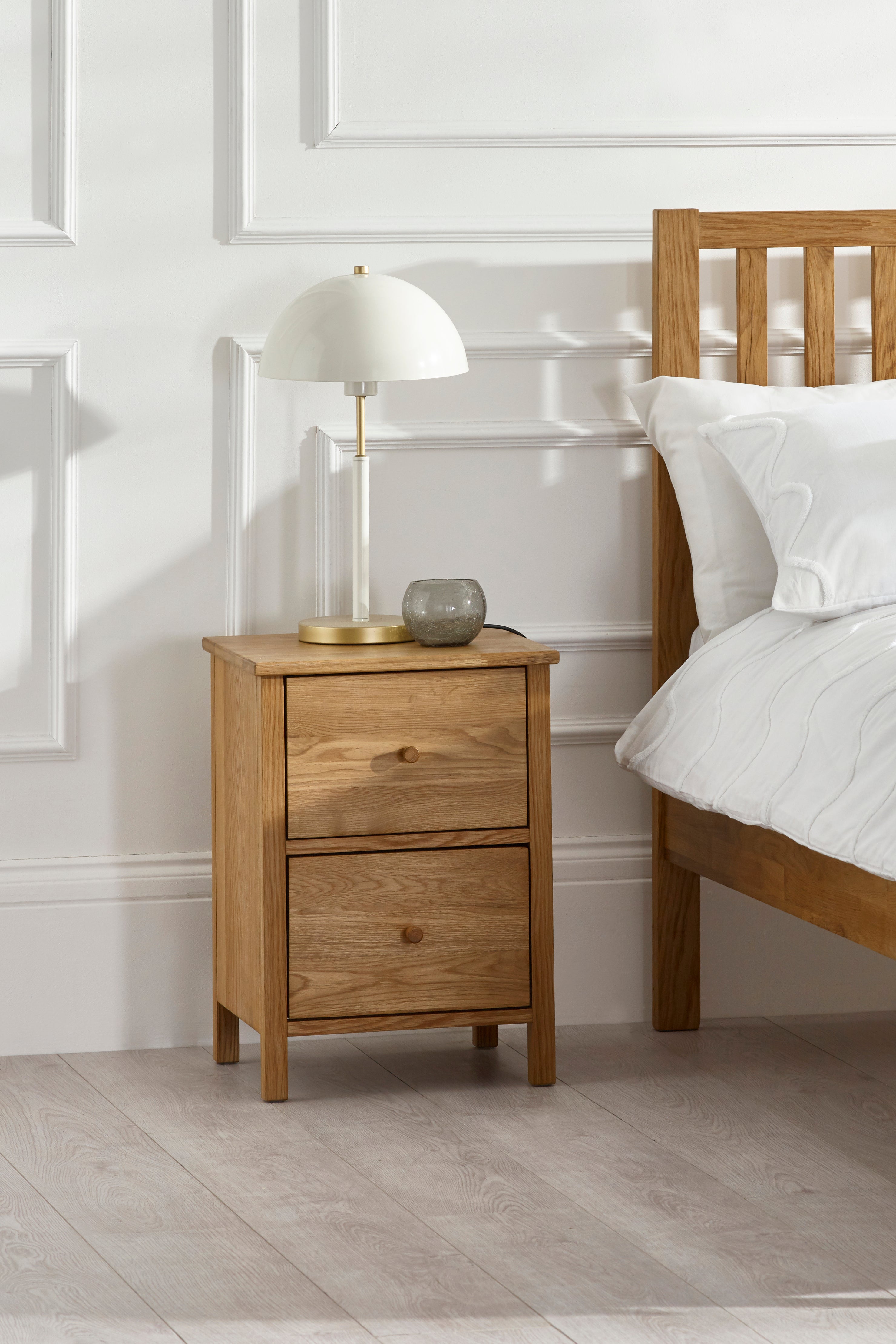 Wooden bedside table with lamp and decor next to a bed in a bedroom setting.
