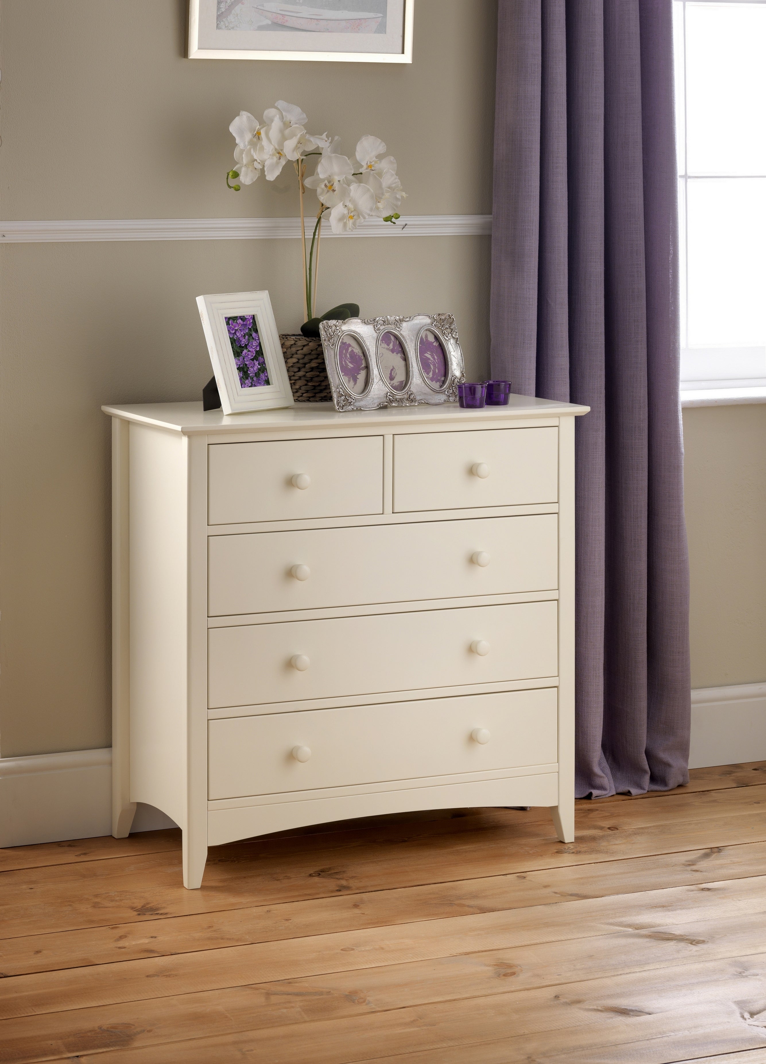White dresser with decorative items against a neutral wall with a purple curtain.