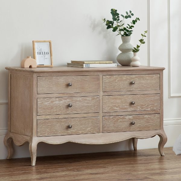 Wooden dresser with four drawers, a vase, and books on top against a white wall.