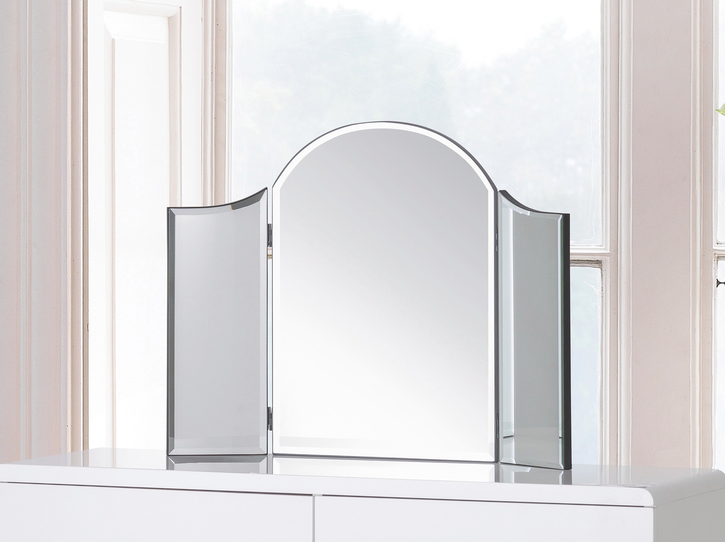 Tri-fold vanity mirror on a white dresser with a neutral background