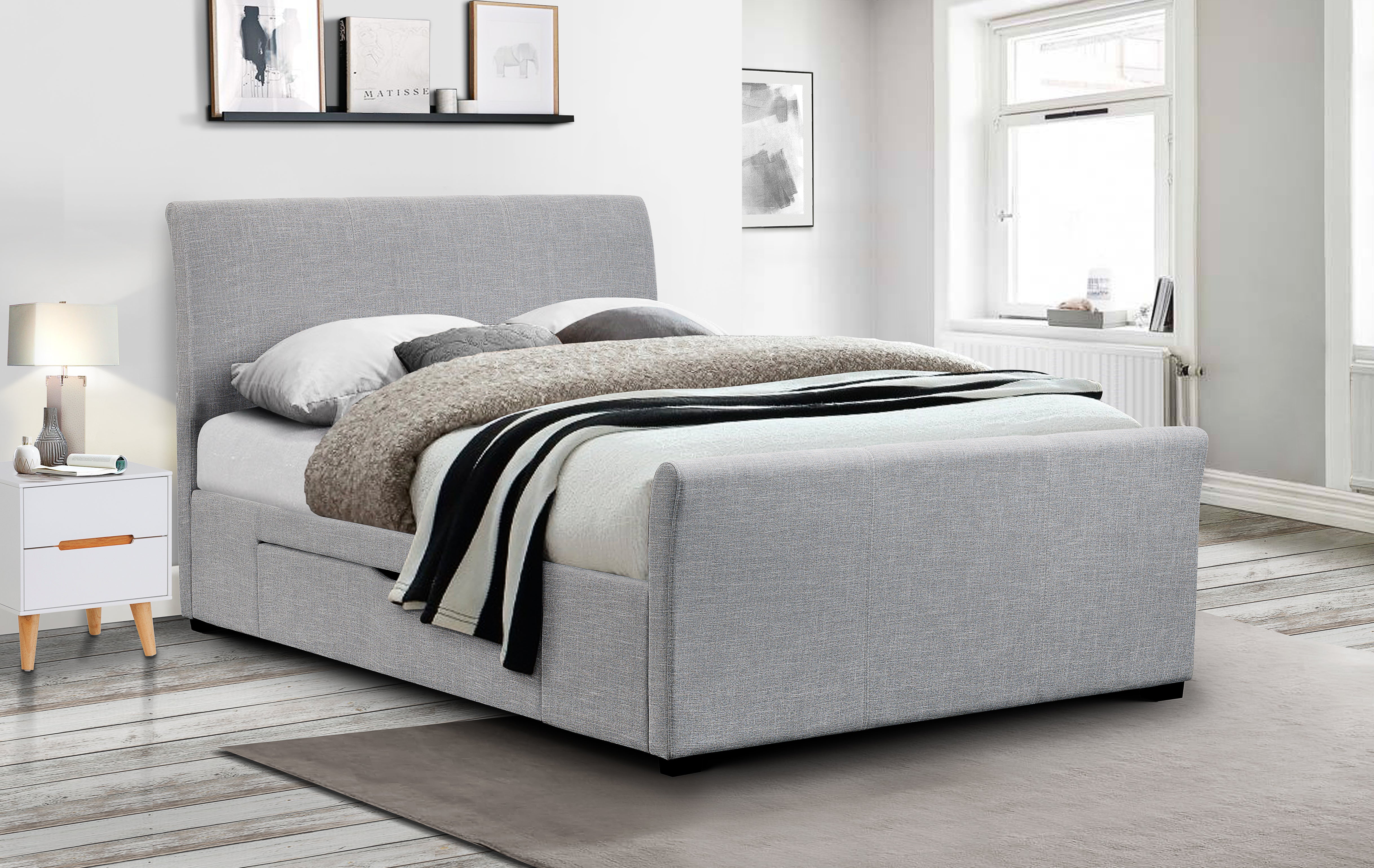 Gray upholstered bed in a room with a nightstand and lamp.