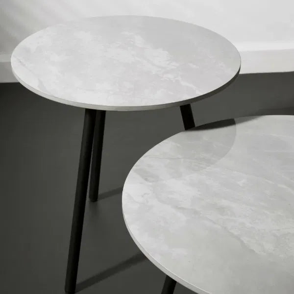 Two round side tables with marble-like tops and black legs on a dark surface.