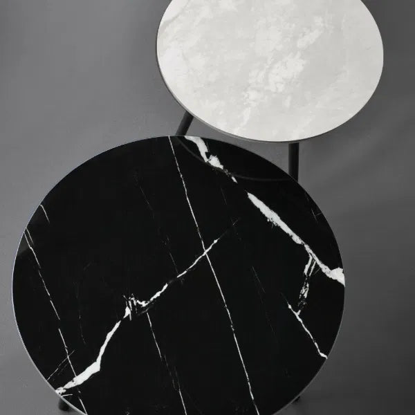 Two round marble tables, one black and one white, on a dark surface.