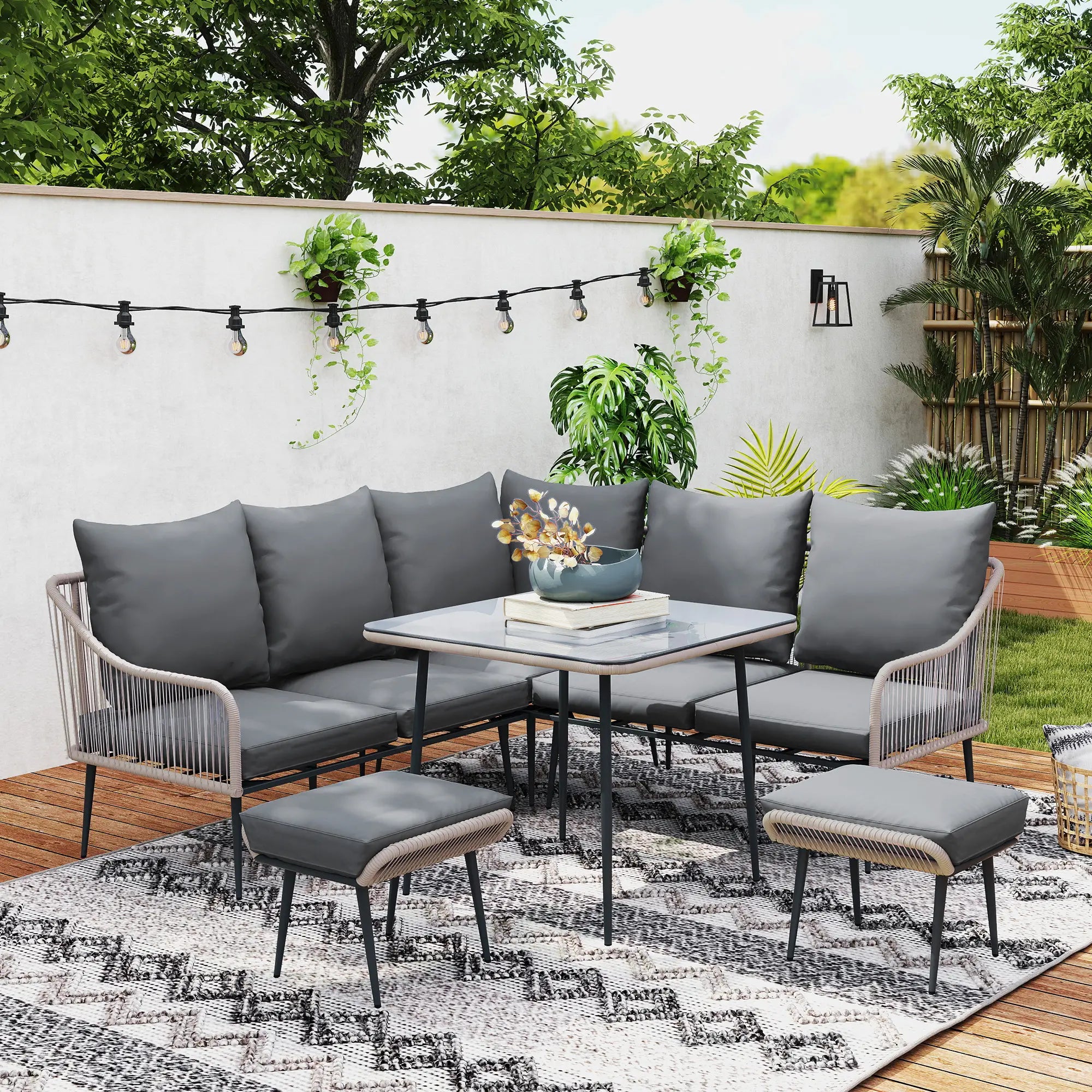 Outdoor patio set with gray cushions on a rug, surrounded by plants and string lights.