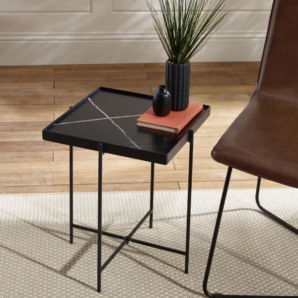 Small black side table with a vase and book next to a brown chair on a wooden floor.