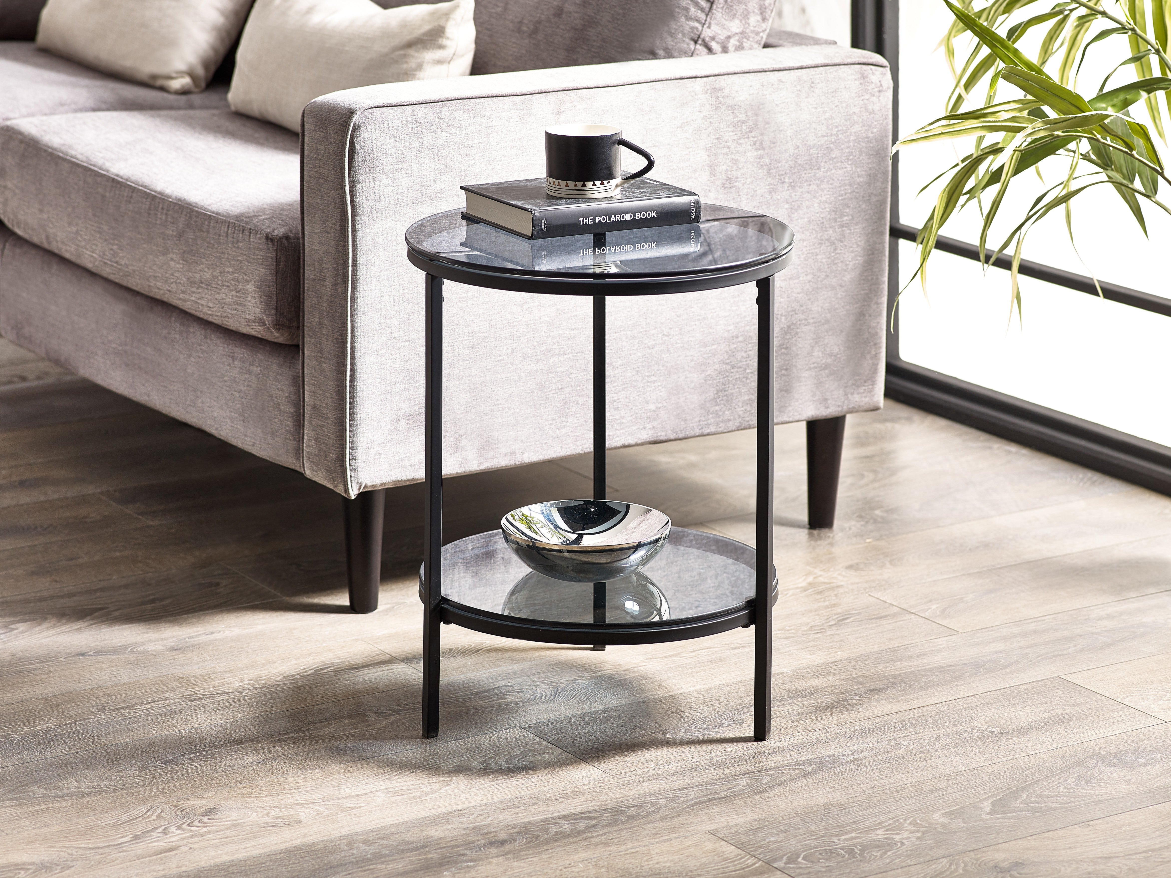 Round glass side table with black metal legs in a living room setting.