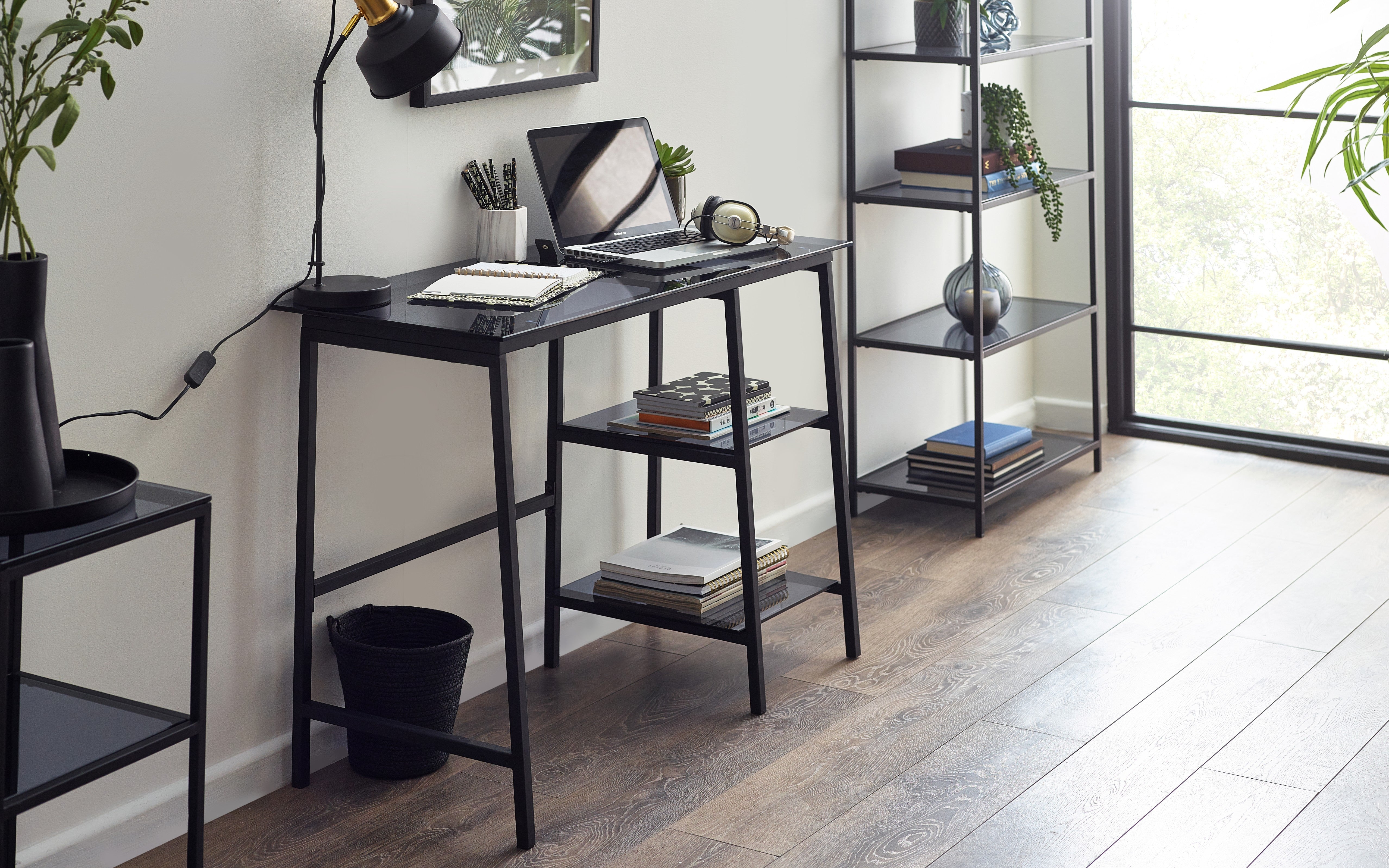 Modern home office with a black desk, laptop, and shelves.