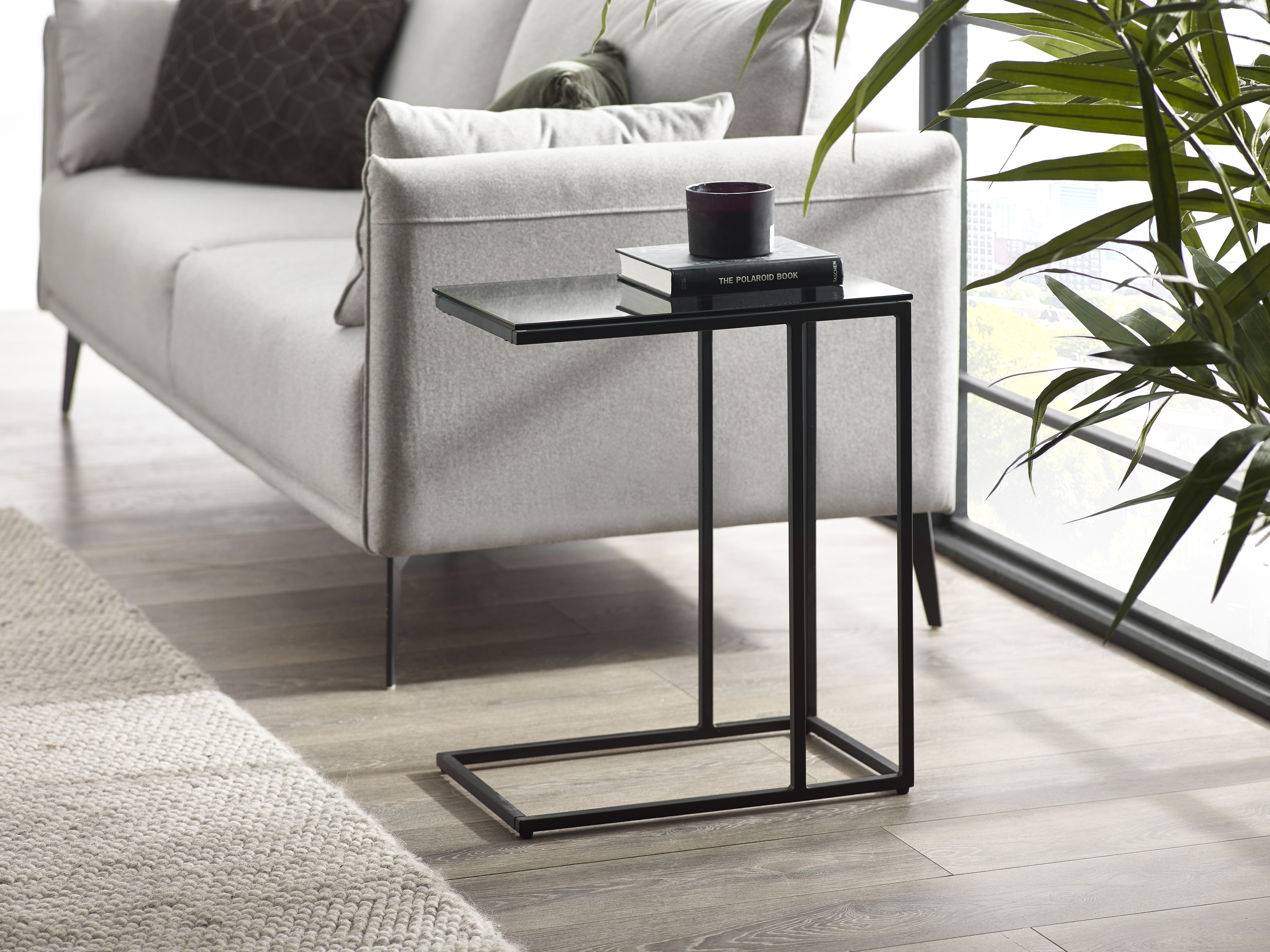 Black side table with a book and cup in front of a white sofa in a living room.