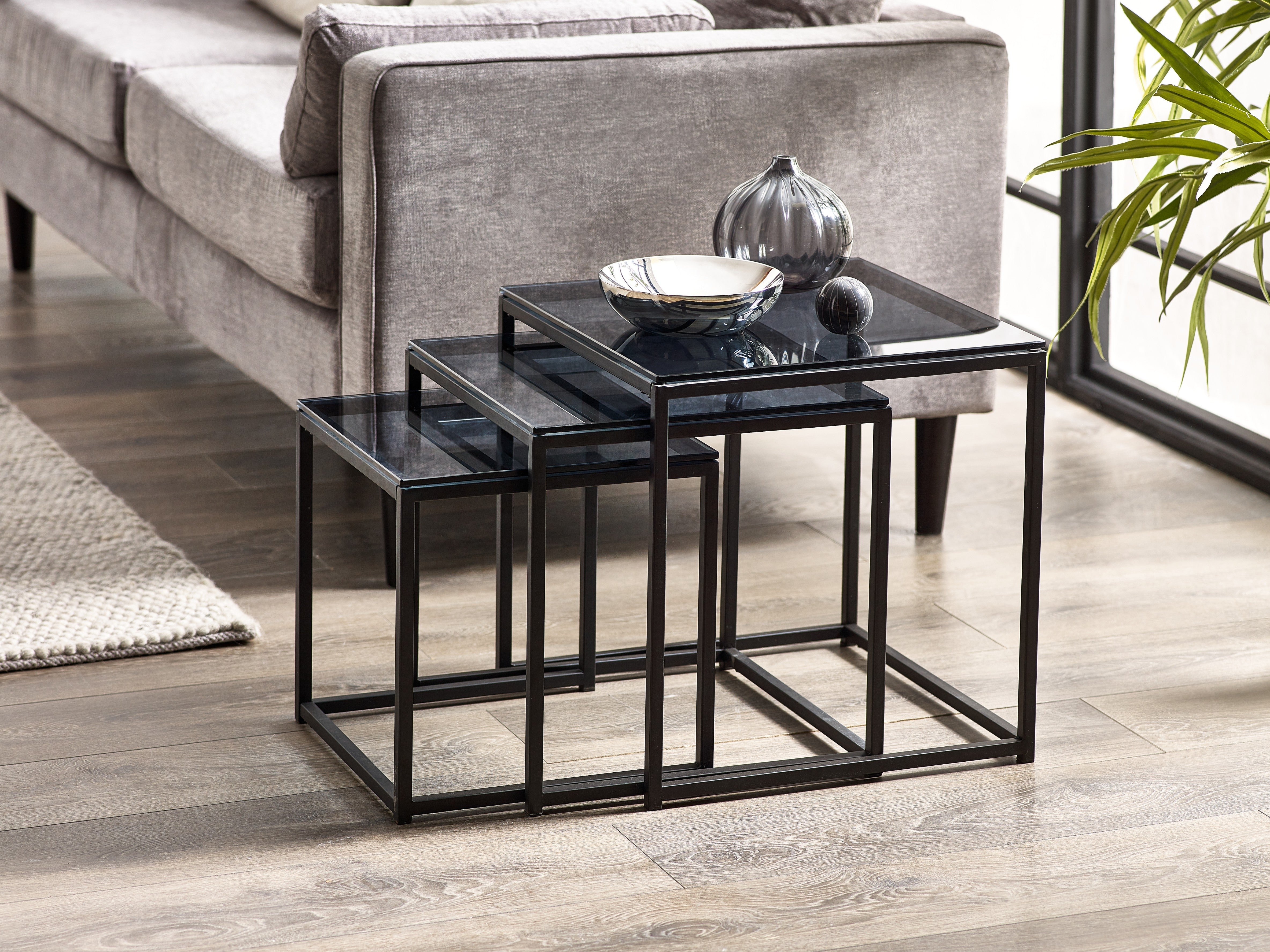 Set of three black glass tables in a living room setting.