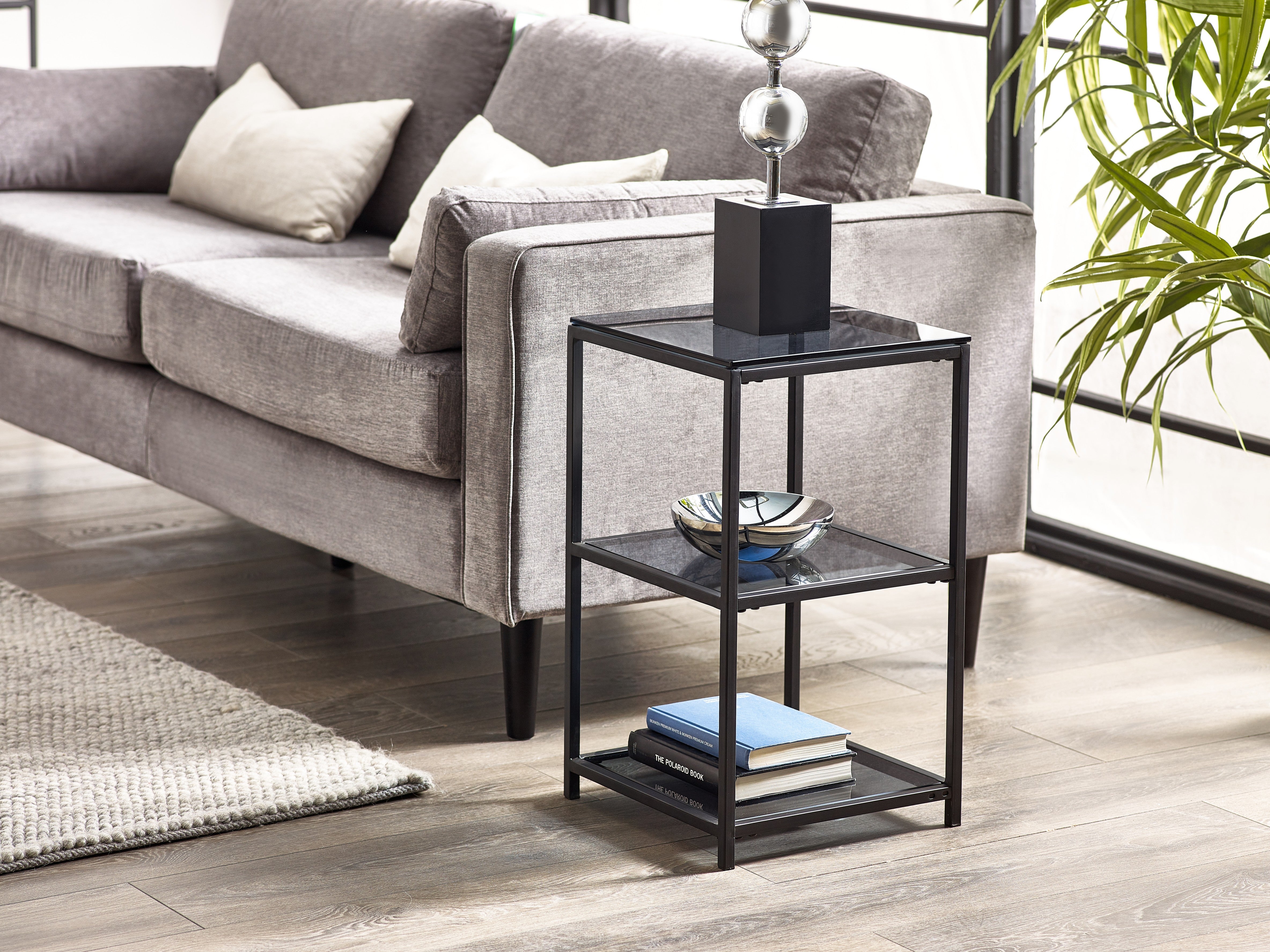 Black three-tier side table in front of a gray sofa with decorative items on it.