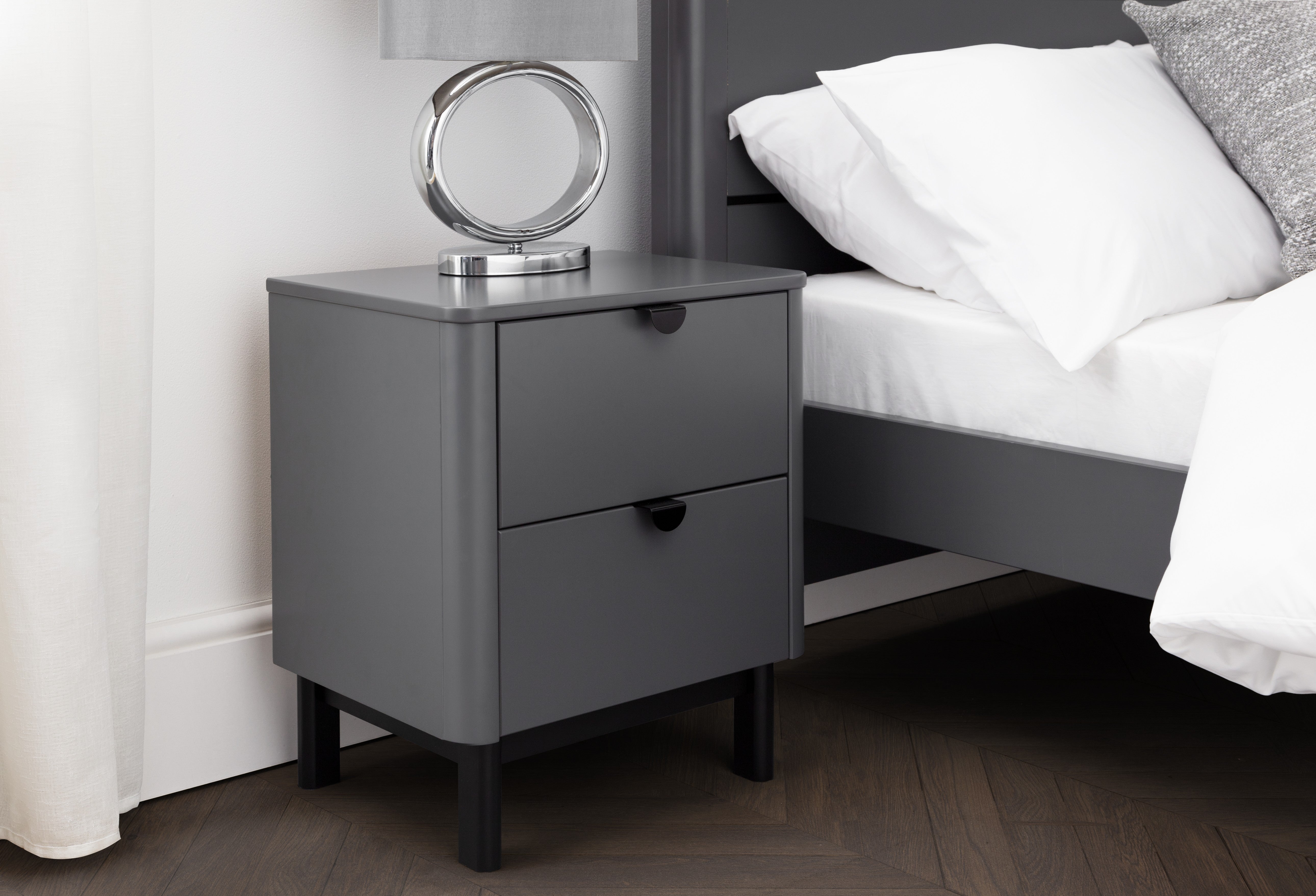 Gray nightstand with a lamp next to a bed with white bedding.