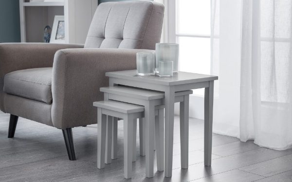 Gray nesting tables in front of a gray armchair with white curtains in the background