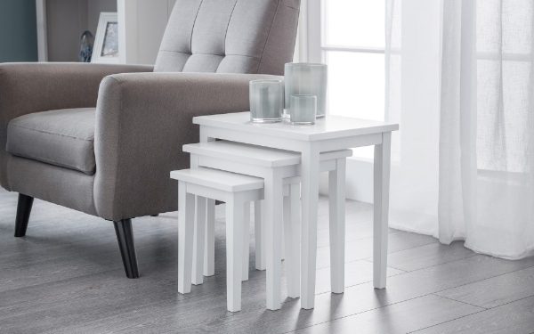 White nesting tables in a living room setting with a gray armchair and light curtains.