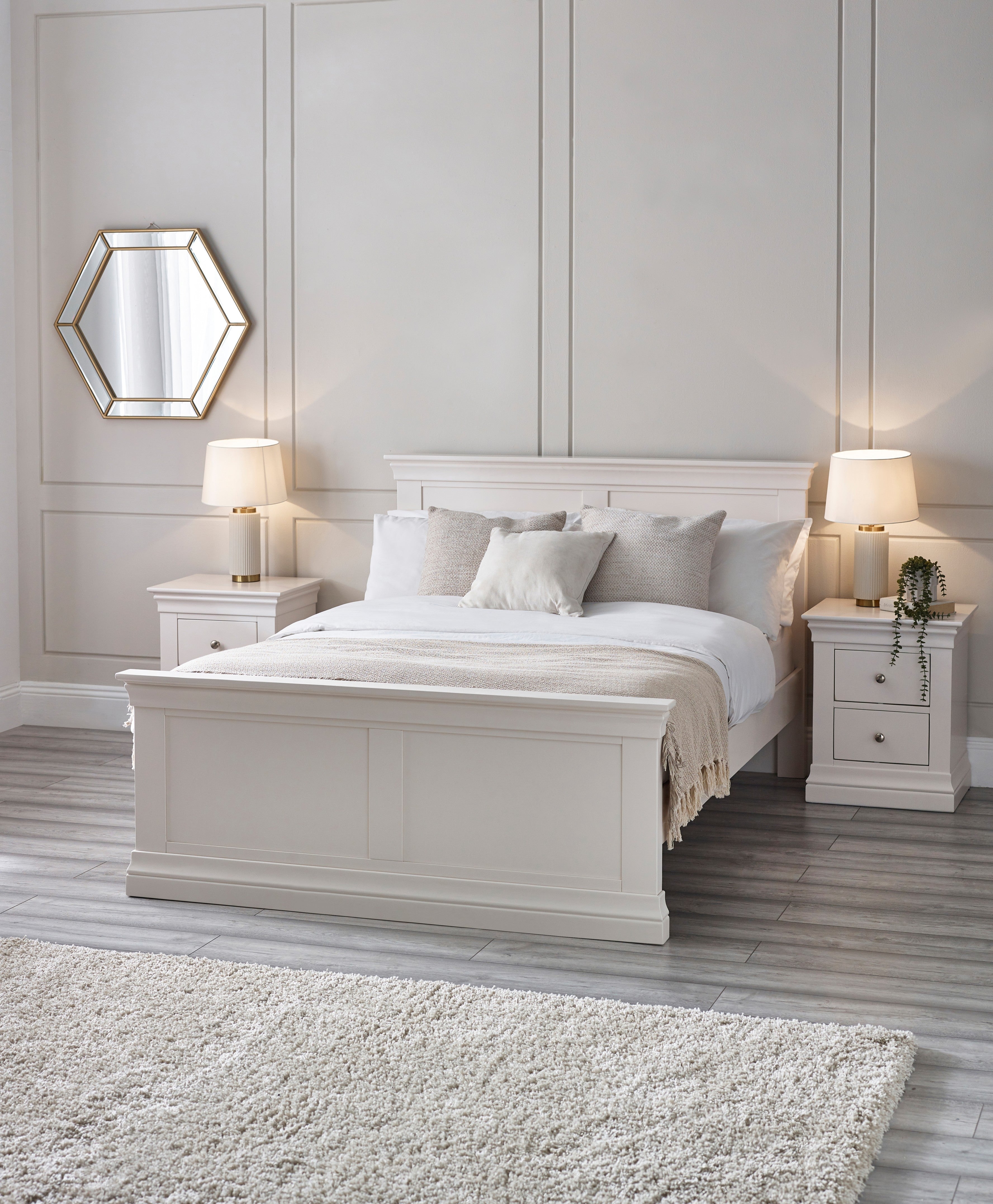 Neatly made bed in a bedroom with white walls, nightstands, and lamps.