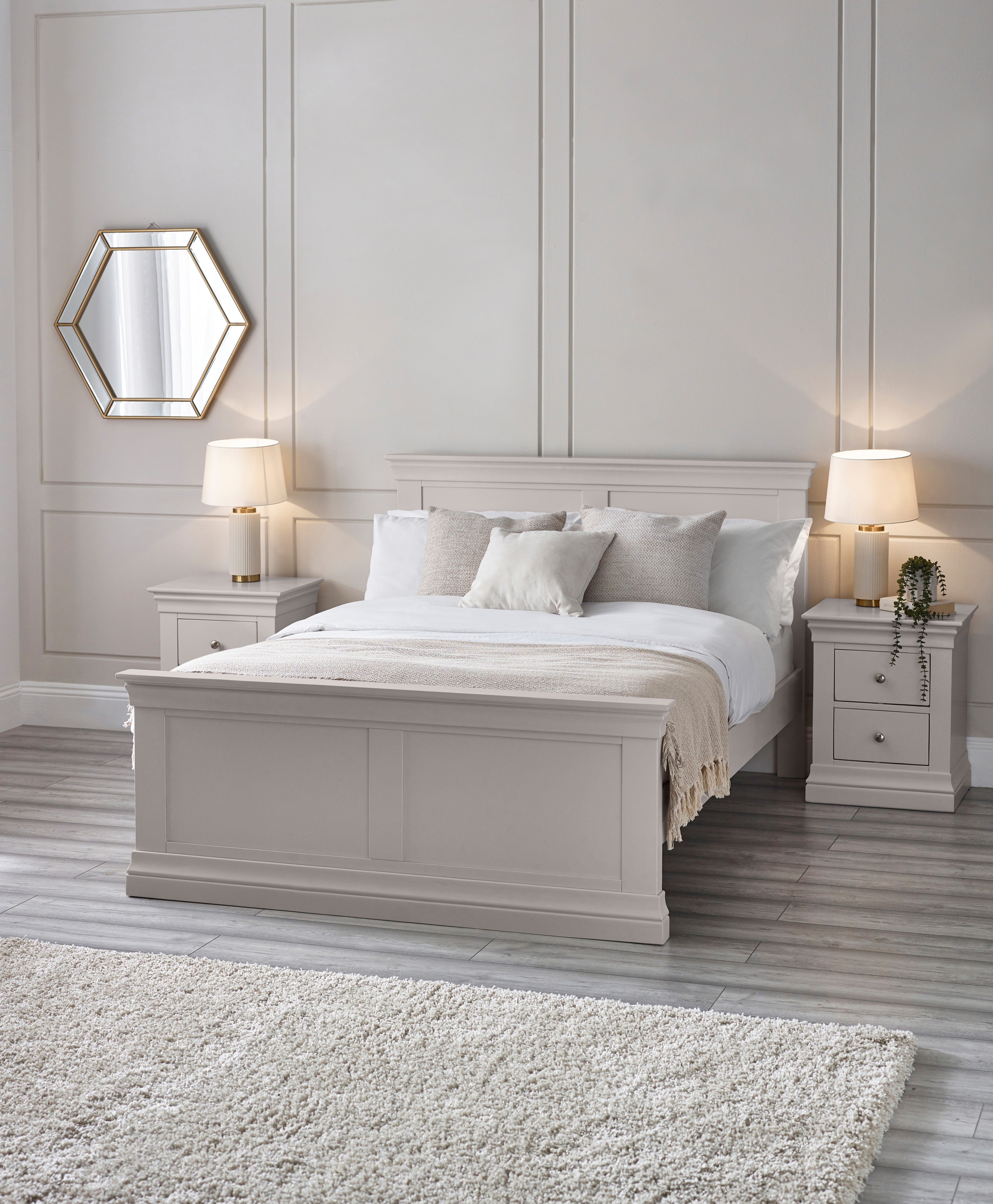 Neatly made bed in a bedroom with white walls, nightstands, and lamps.